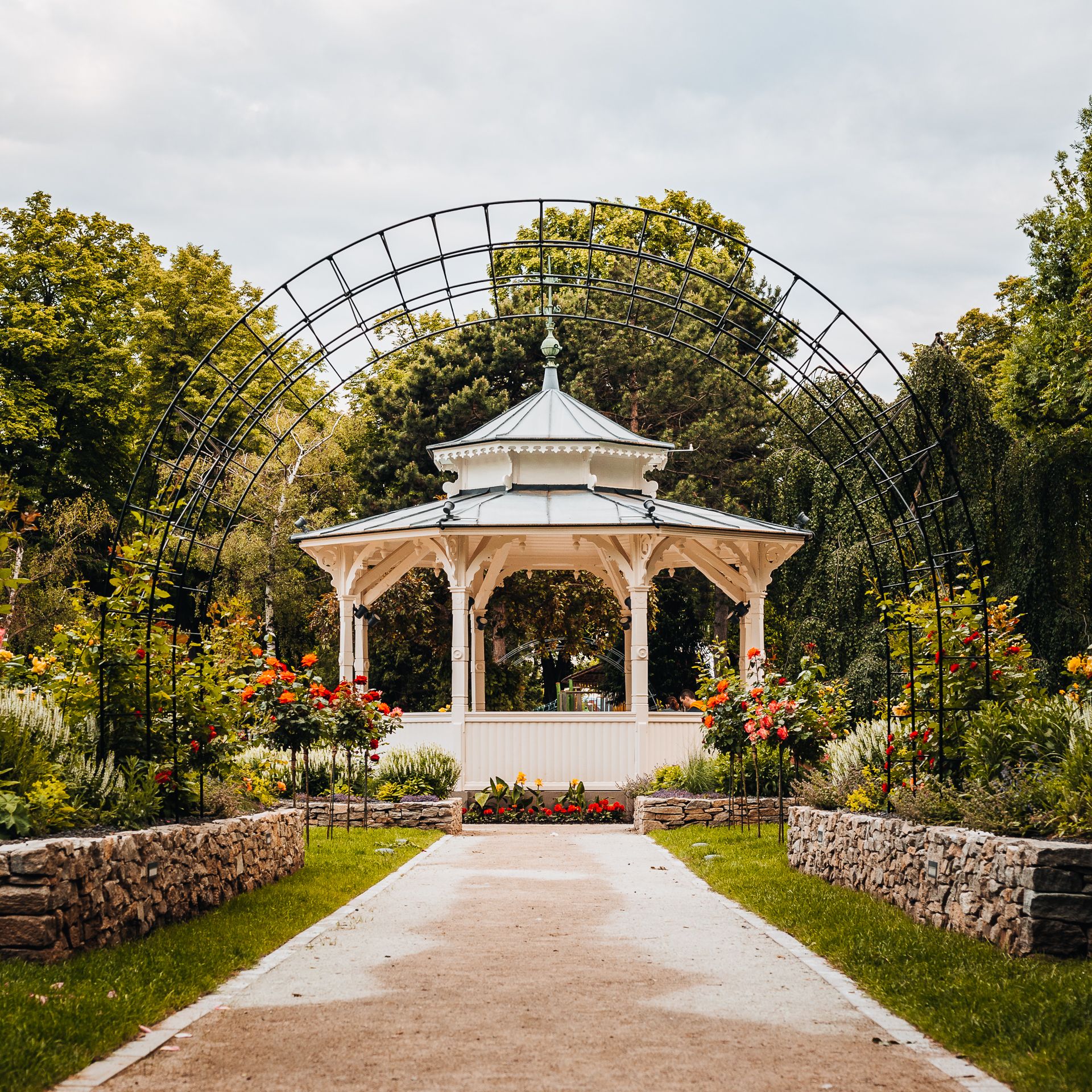A green city park with a romantic pavilion, a rose garden, and a trellised arch