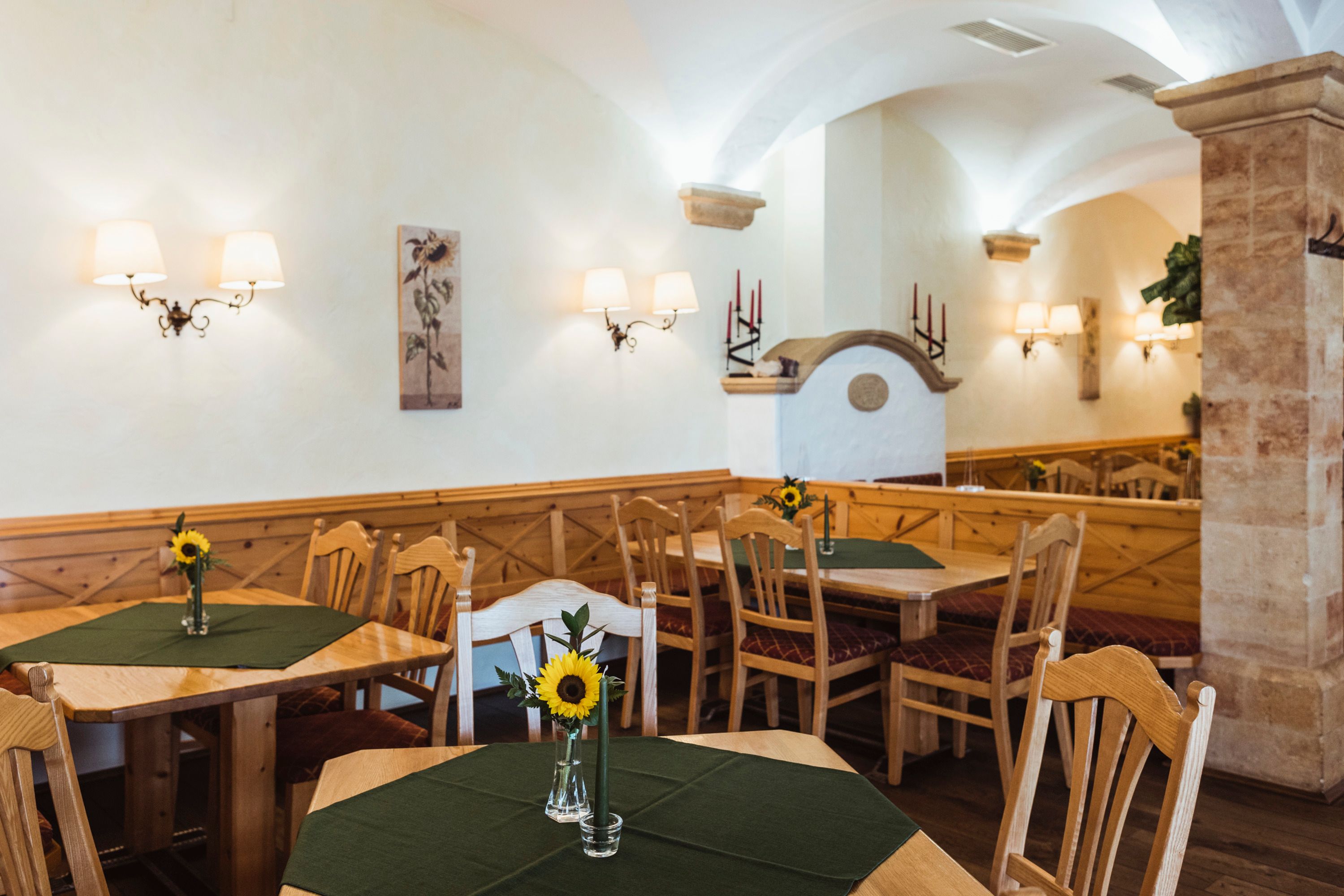 Cozy pub with wooden furniture, green tablecloths and sunflowers in vases.