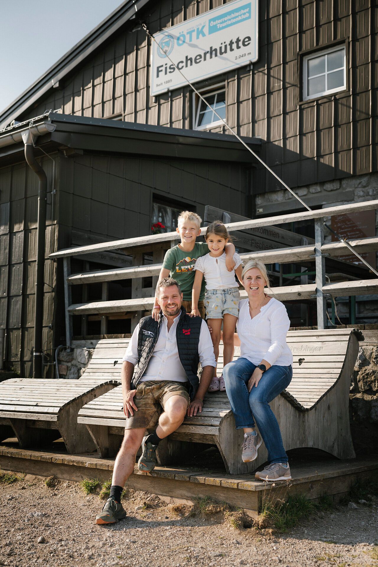 A family is sitting on a wooden bench in front of the fisherman's cabin on Schneeberg
