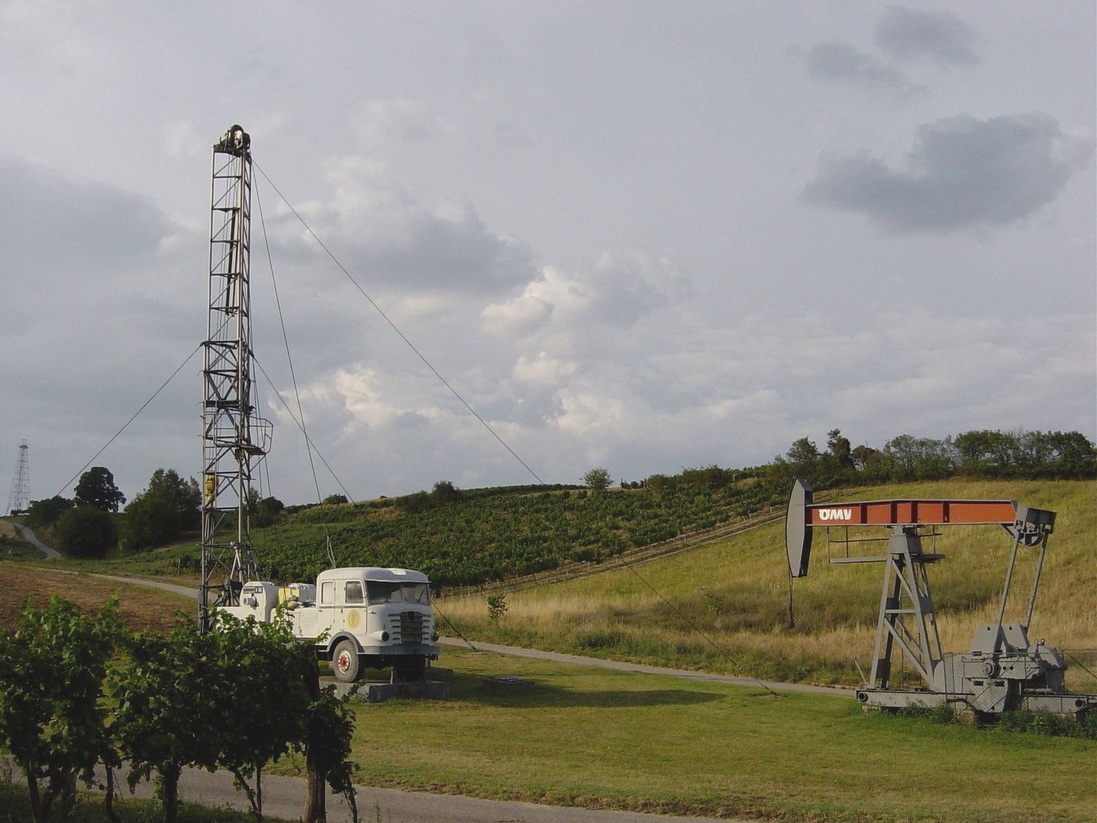 Oil pump and drilling rig in a rural setting.