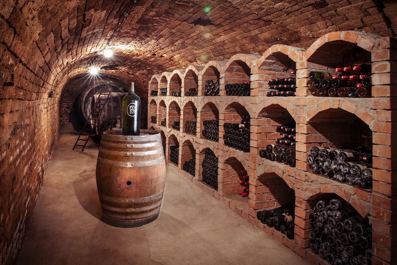 Wine cellar with brick vaults, wine racks and a barrel with a large bottle.