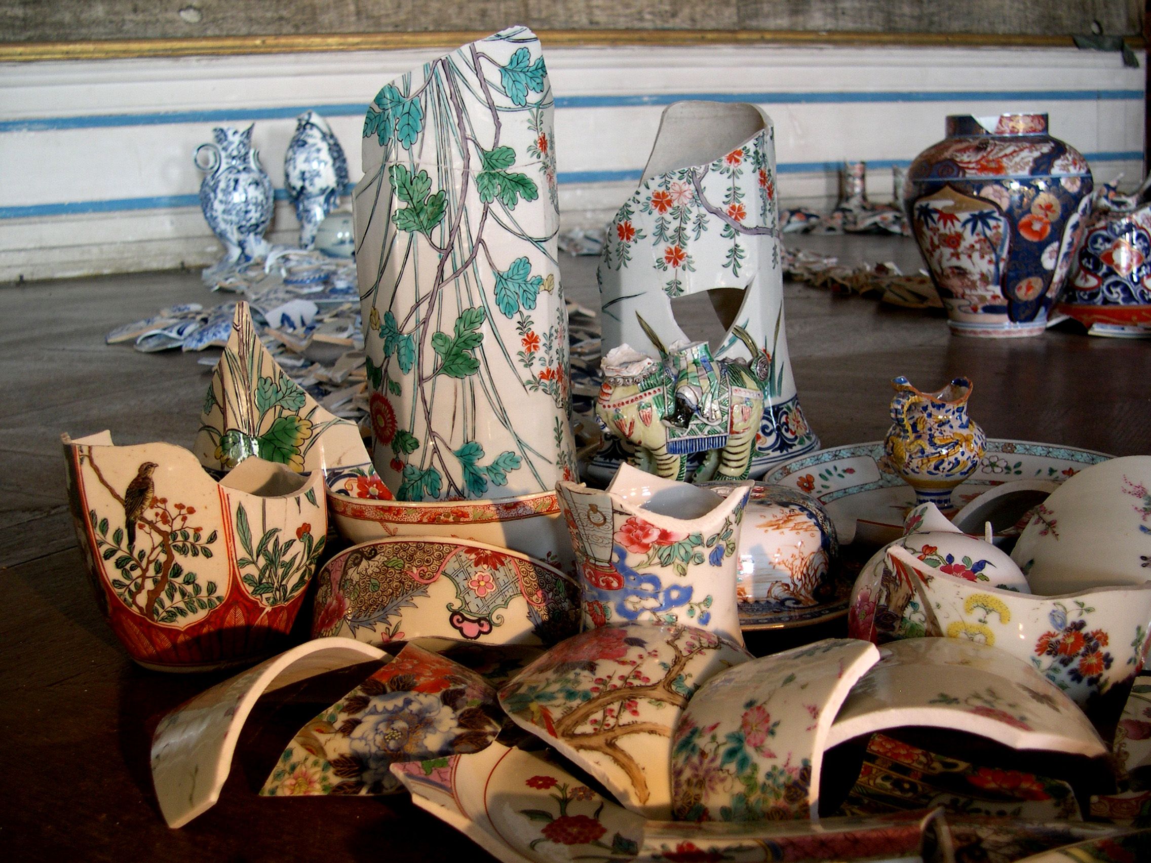 Broken pieces of porcelain with colorful patterns arranged on a floor.