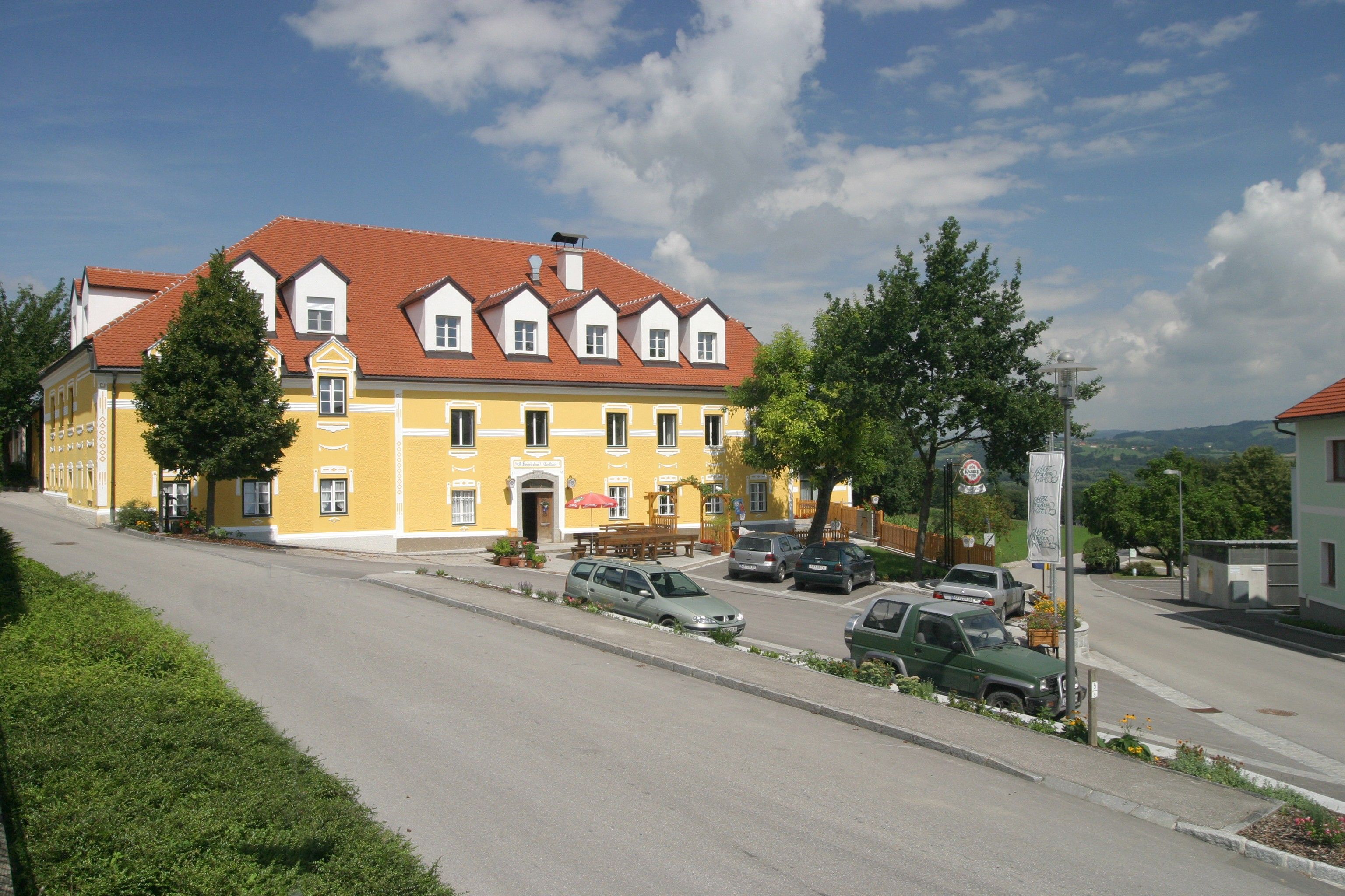 A yellow building with a red roof, surrounded by cars and trees, under a blue sky.