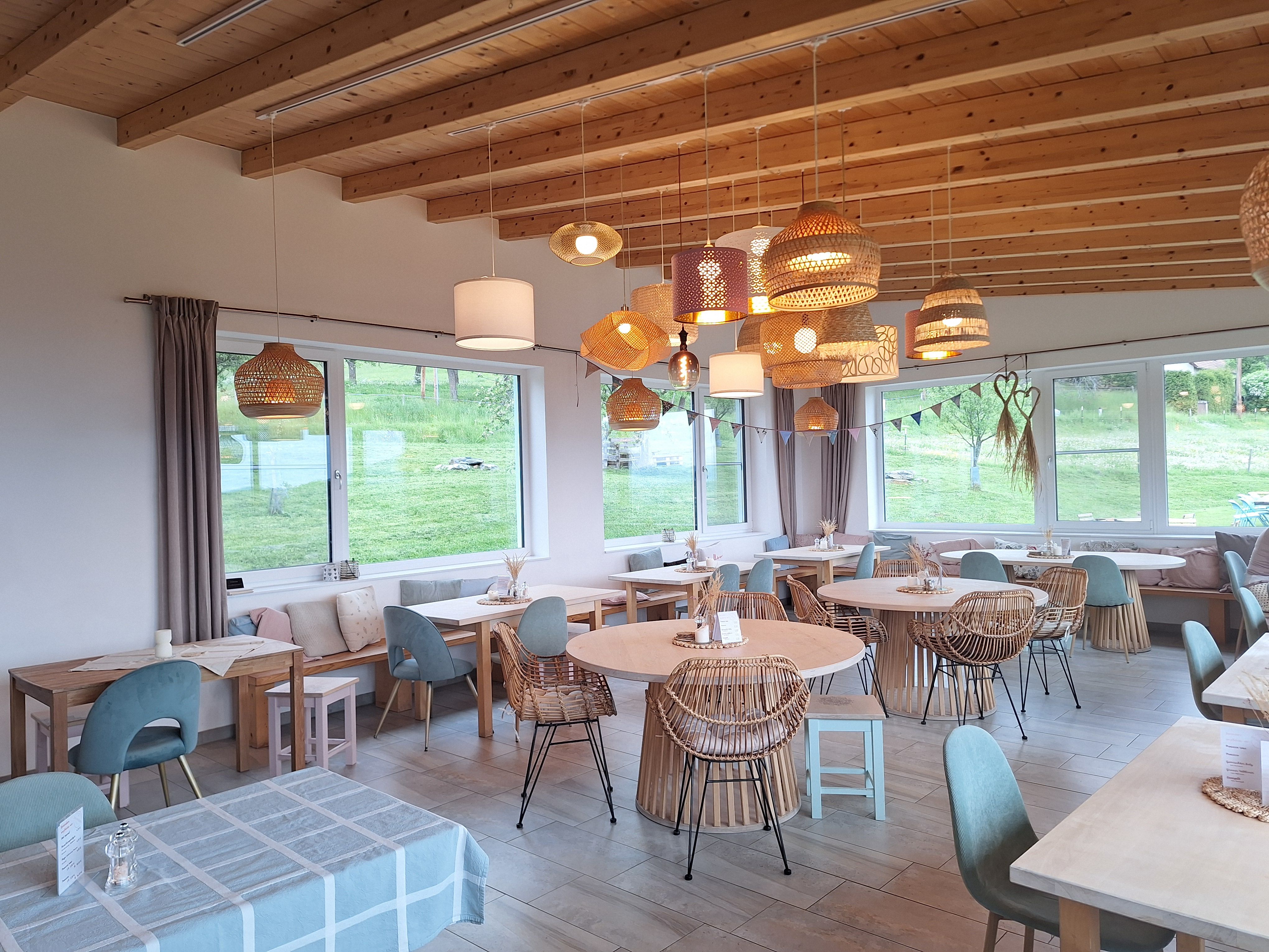 Cozy dining room with wooden furniture and hanging lamps, large windows with a view of the greenery.