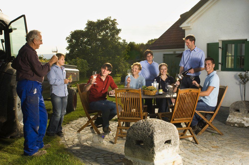 Group of people sitting outside at a table with wine and snacks.