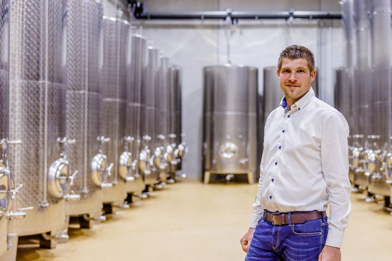 A man stands in a room with large stainless steel tanks.