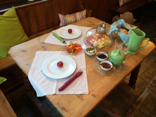 A laid breakfast table with plates, cutlery, cold cuts, vegetables and drinks.
