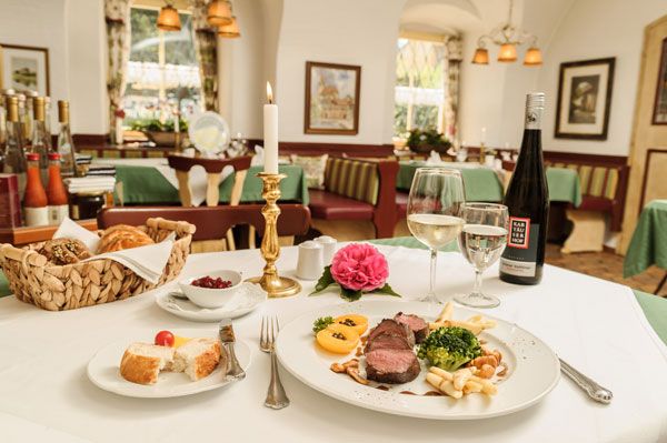 Elegant restaurant with laid table, candle, bottle of wine and plate with meat dish.