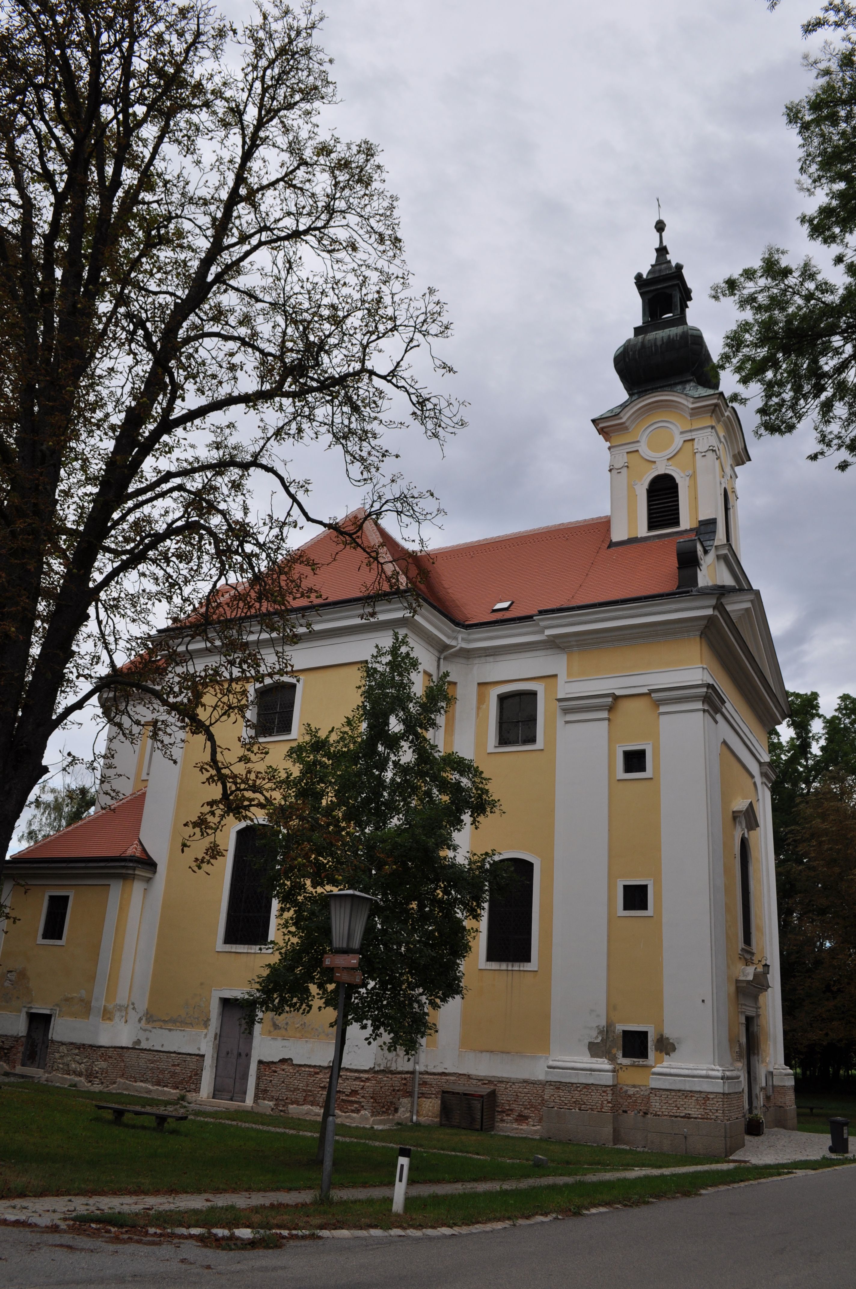 Yellow church with red roof and tower, surrounded by trees.