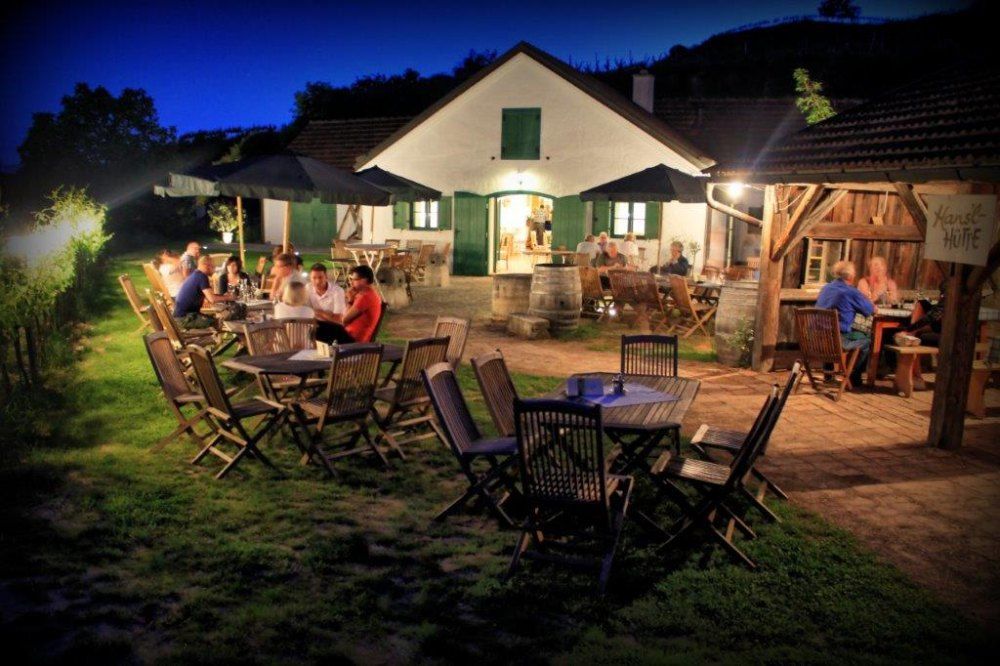 Evening scene in a wine tavern with guests at wooden tables outdoors.