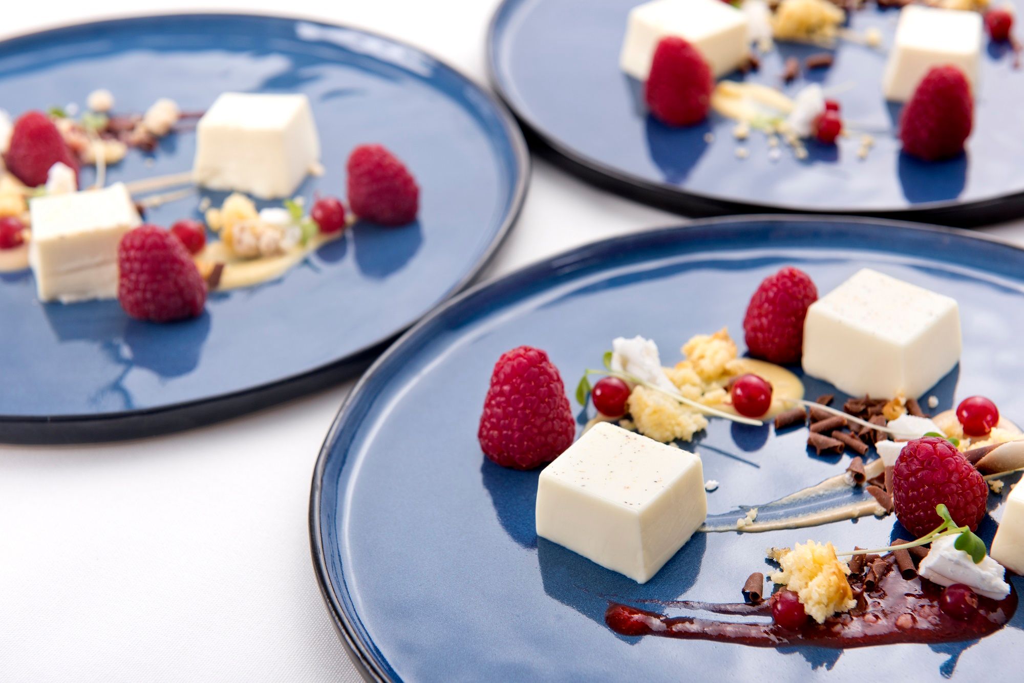 Elegant dessert presentation on blue plates with raspberries, cream and chocolate chips.