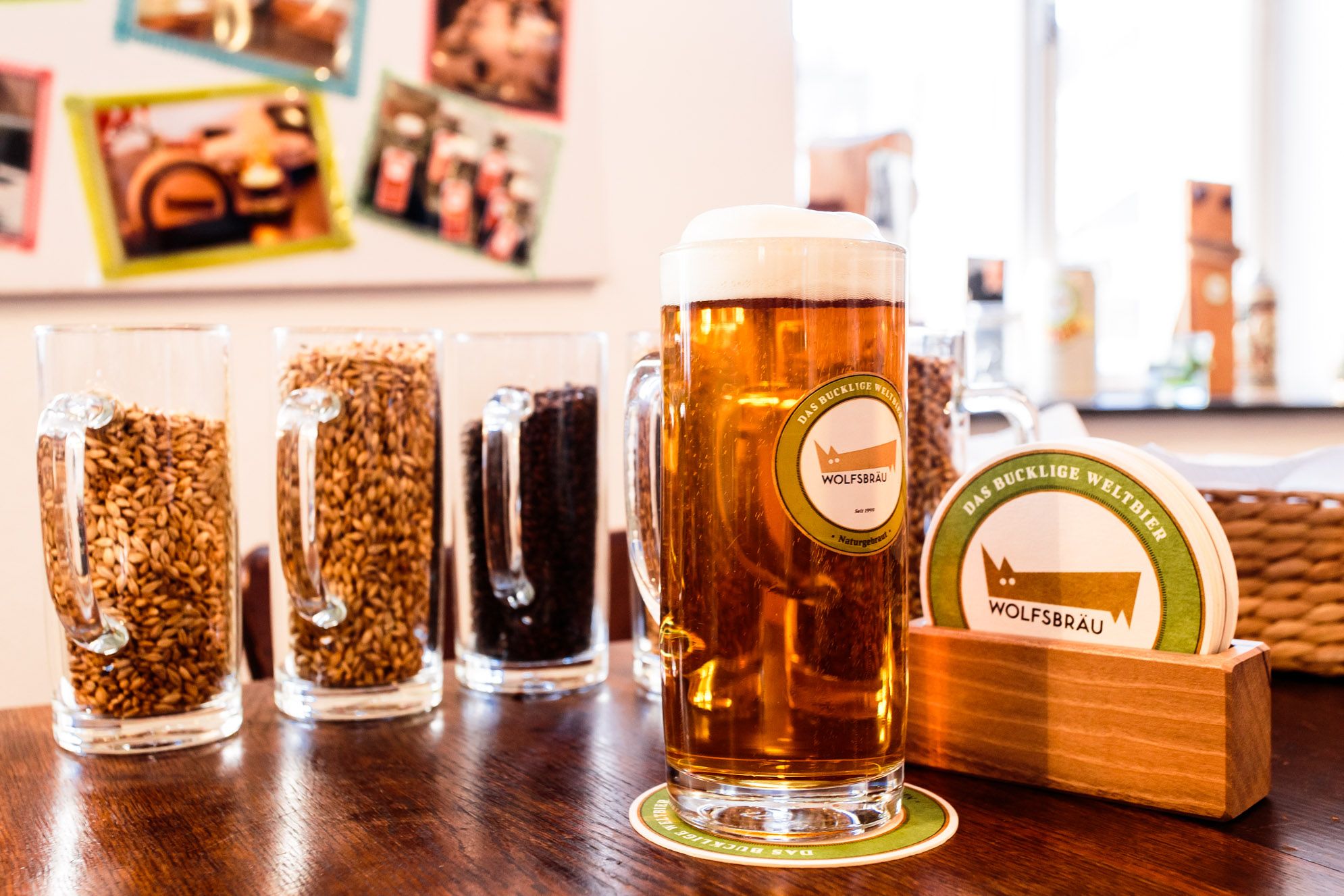 Mug with beer next to beer mats, in the background beer glasses with grain.