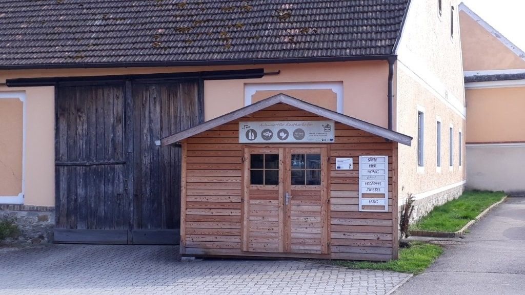 A small wooden store in front of a large building with a wooden gate.