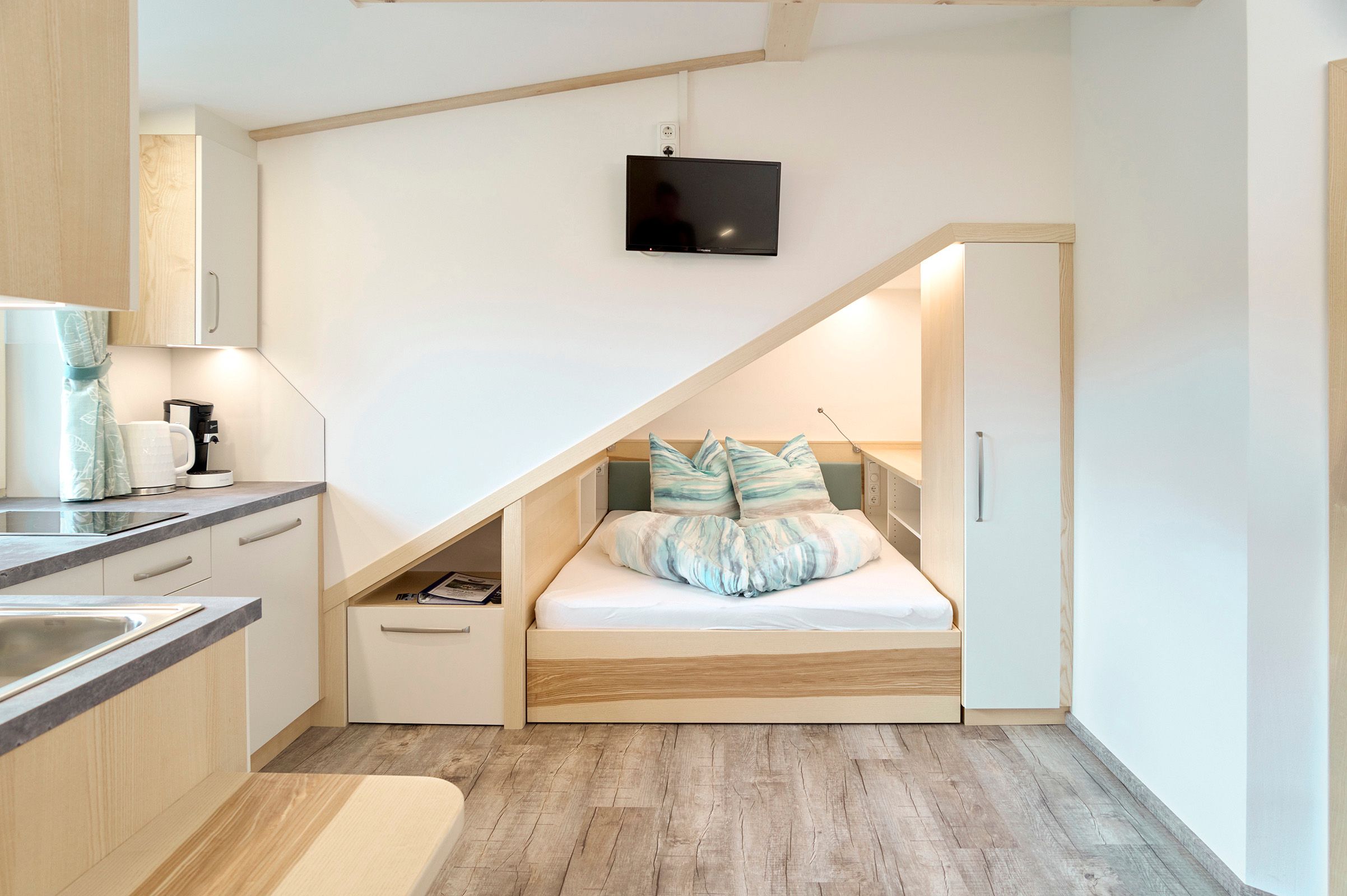 Compact apartment with integrated bed under a sloping roof, kitchenette and TV.