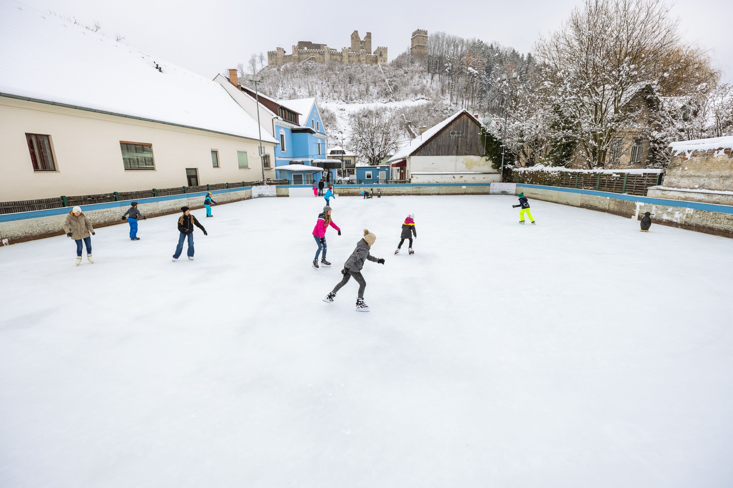 People skating on a square in Kirchschlag, with a castle ruin on a hill in the background.