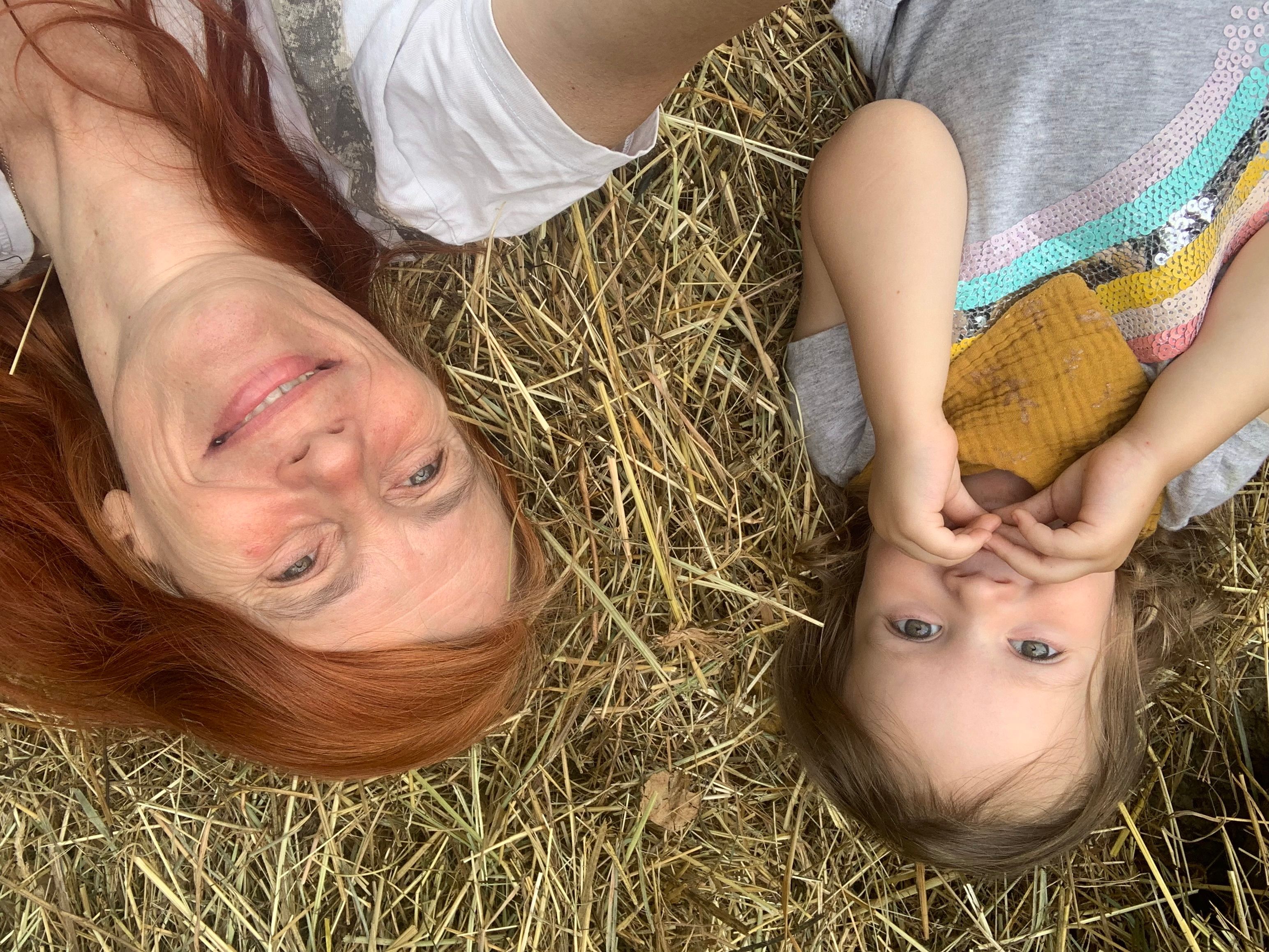 Two people lie smiling on hay, an adult and a child.