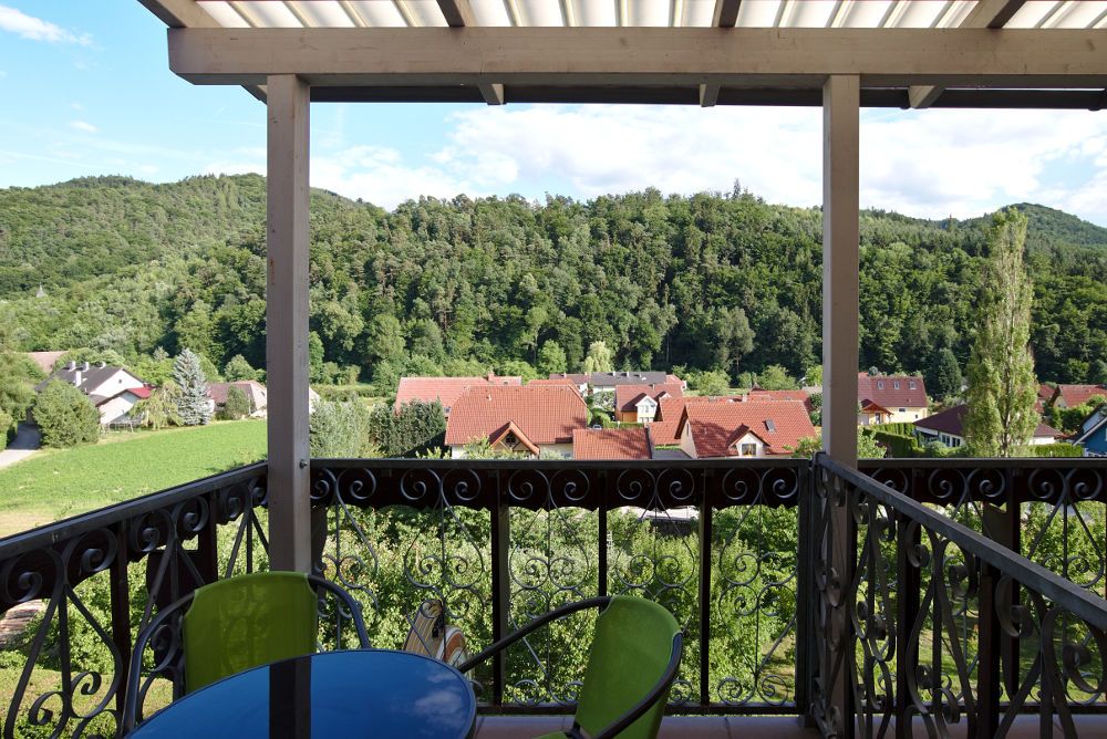 View from a balcony of a green landscape with hills and red roofs.