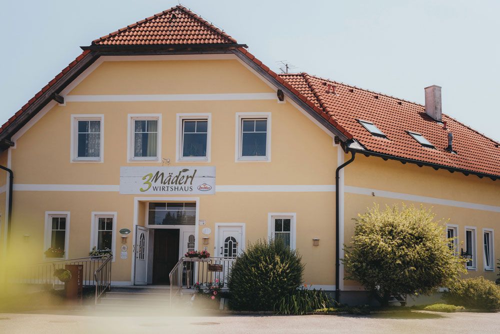 Yellow building with red roof and sign '3 Mädel Wirtshaus'.