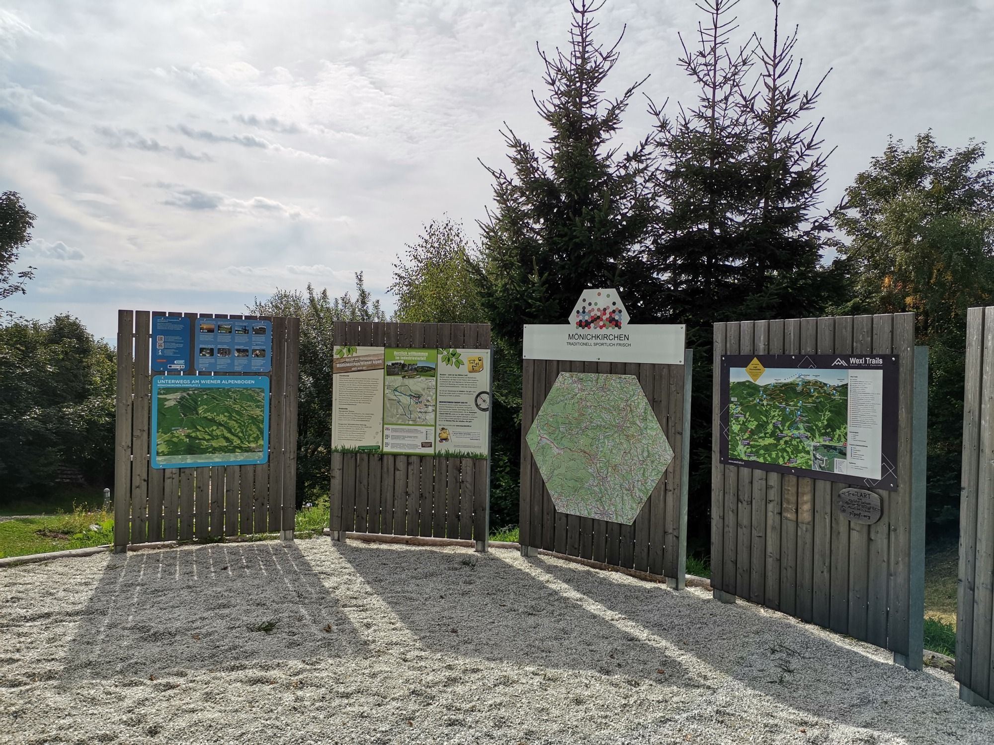 Information boards at the hiking starting point in Mönichkirchen with maps and information, surrounded by trees.