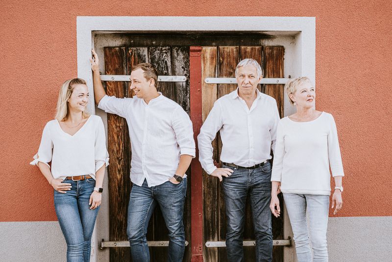 Four people are standing in front of a wooden door, all dressed in white.