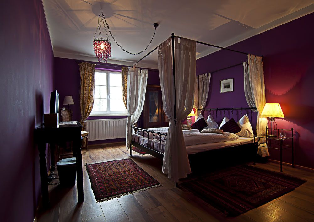 A cozy bedroom with a four-poster bed, purple walls and warm light.