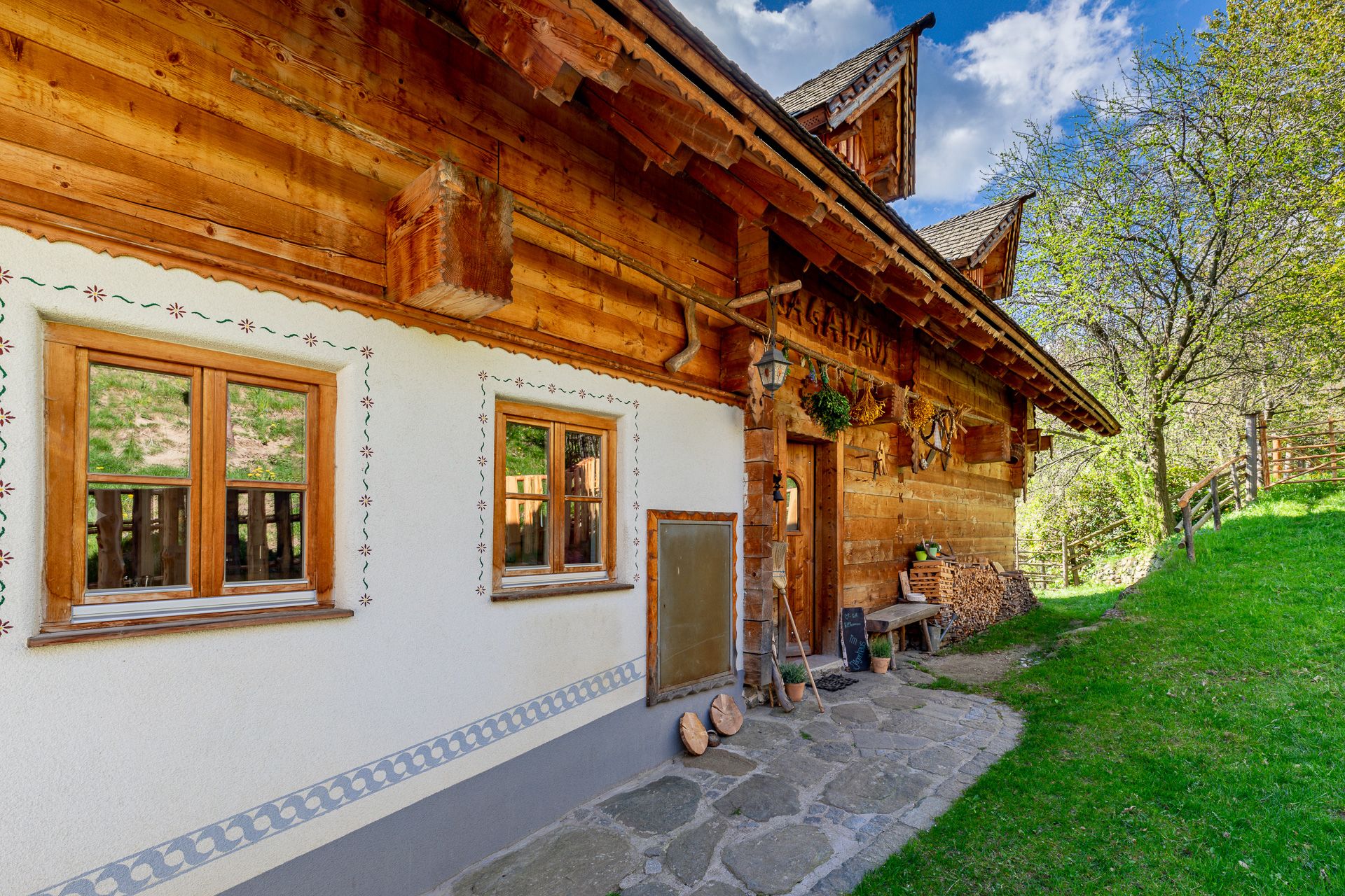 Traditional house with lots of wood, decorative windows and decorations next to a green meadow.