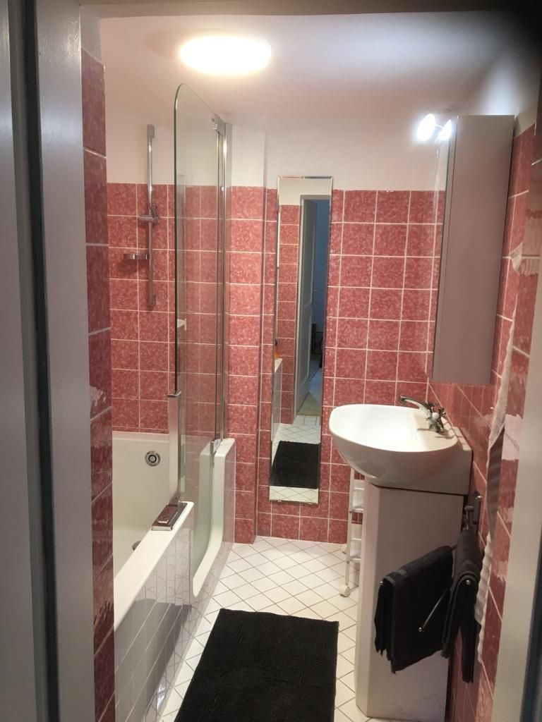 Small bathroom with pink tiles, bathtub, washbasin and mirror.