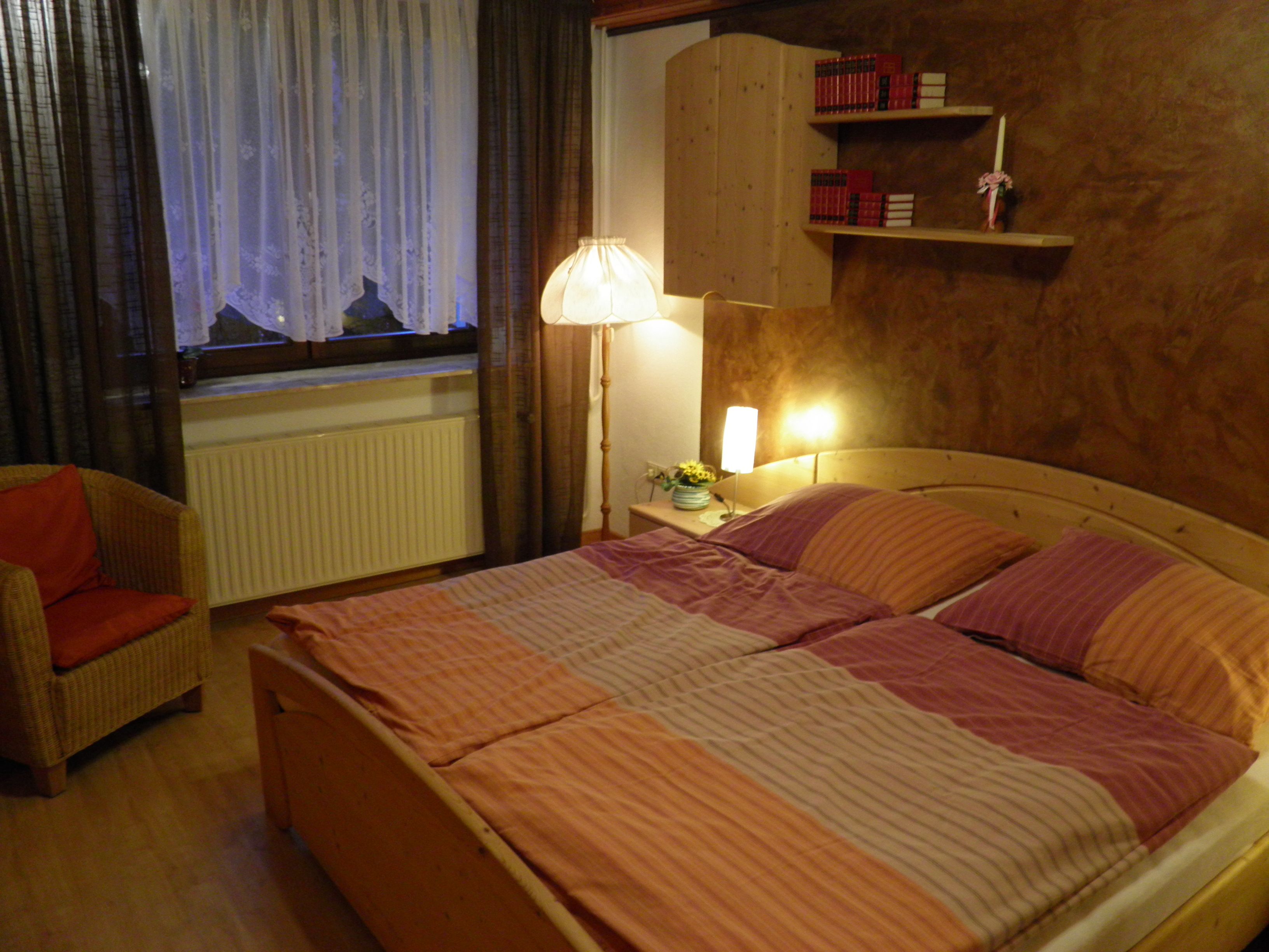 Cozy bedroom with double bed, bedside lamps, bookshelf and armchair.