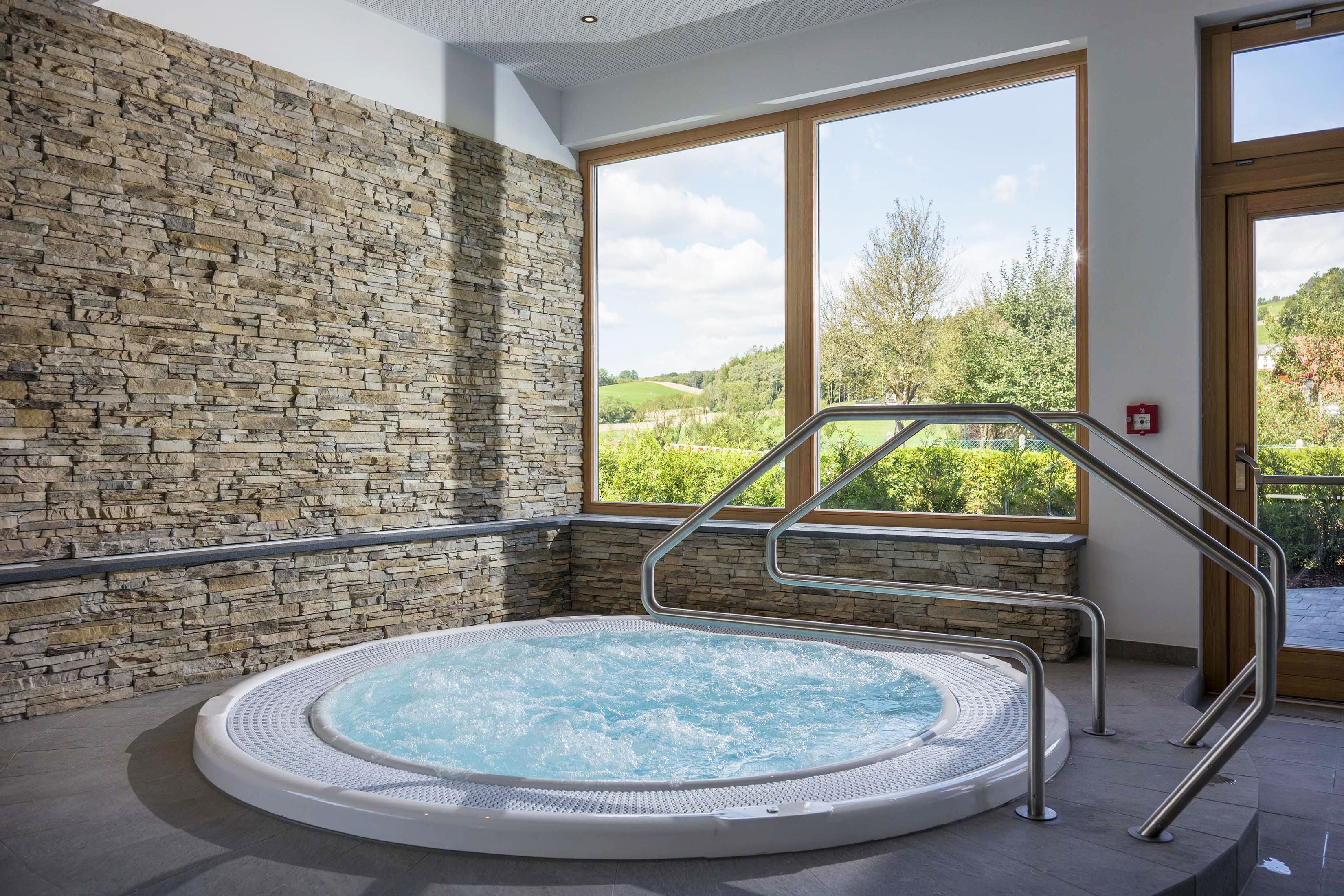 Wellness room with whirlpool, stone walls and large window with a view of the countryside.