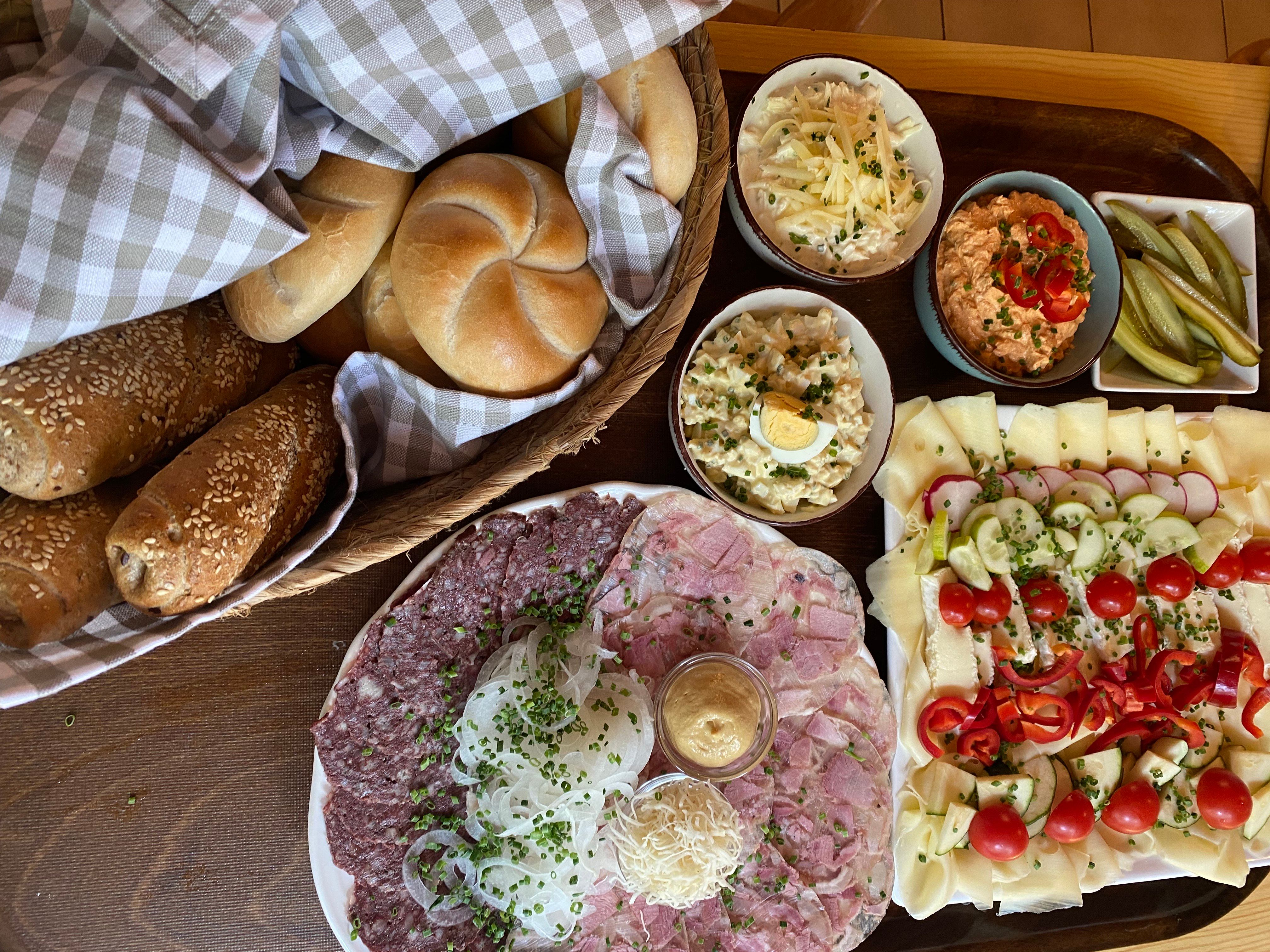 A selection of Austrian snack specialties with bread, cold cuts, cheese, salads and pickled gherkins on a table.