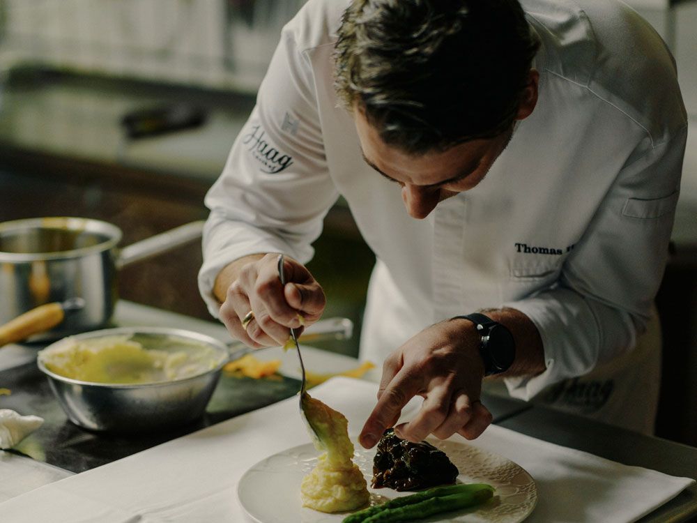 A chef prepares a dish of asparagus and mashed potatoes on a plate.