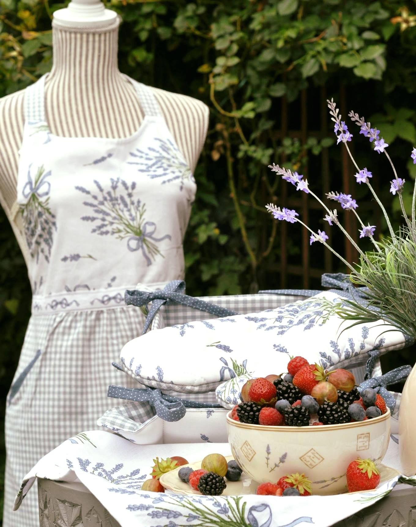A bowl of berries on a table with lavender decorations and a dressmaker's dummy with an apron in the background.