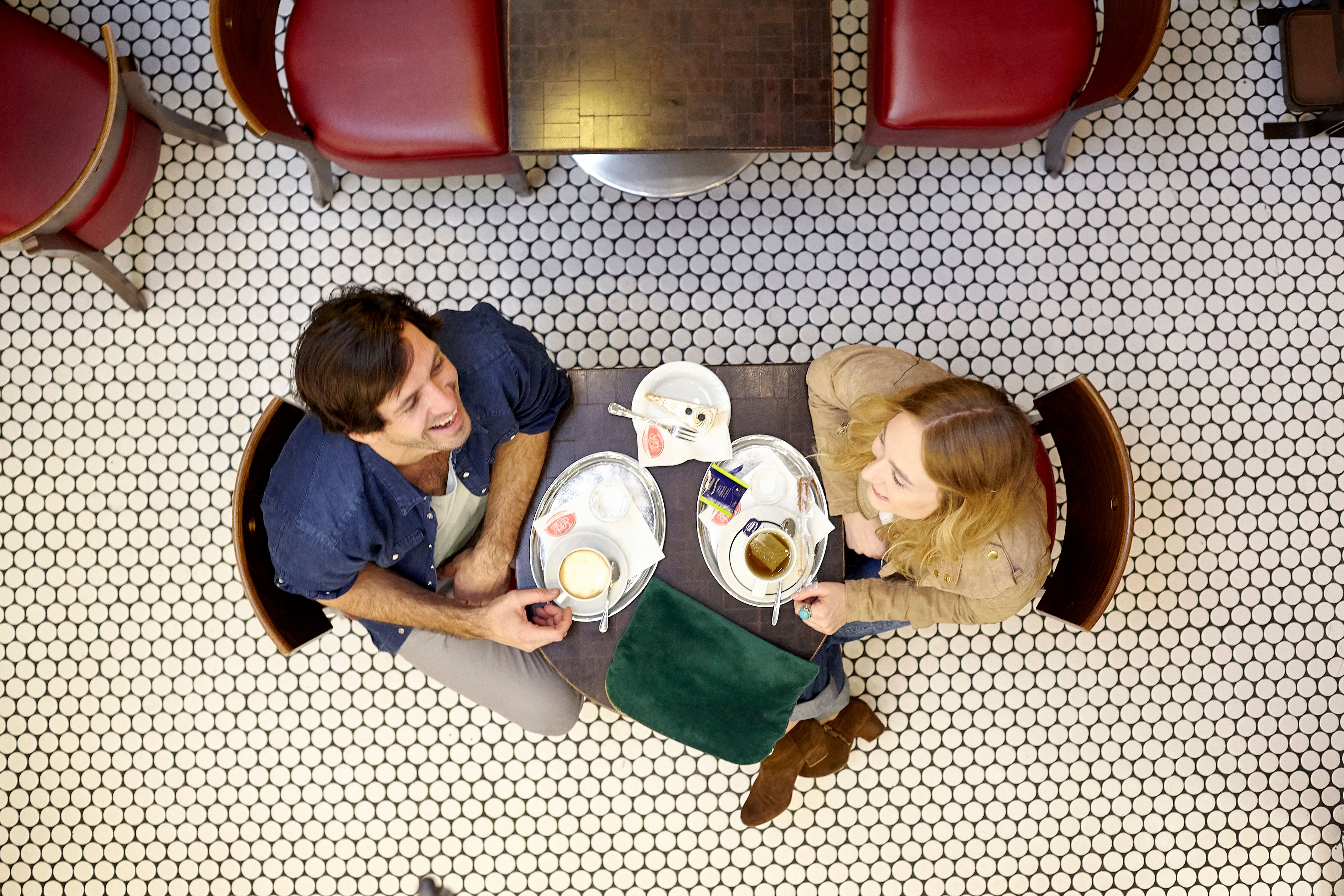A lively main square with cafés and stores, surrounded by historic buildings. People sit outside, a cyclist rides past. Blue sky with clouds.