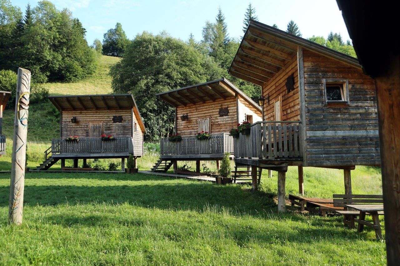 Three wooden huts on stilts with verandas in a green, wooded area.
