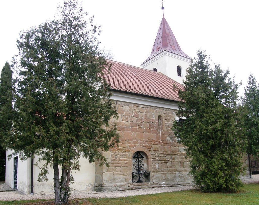 An old church with a red tiled roof and a tower, surrounded by trees.