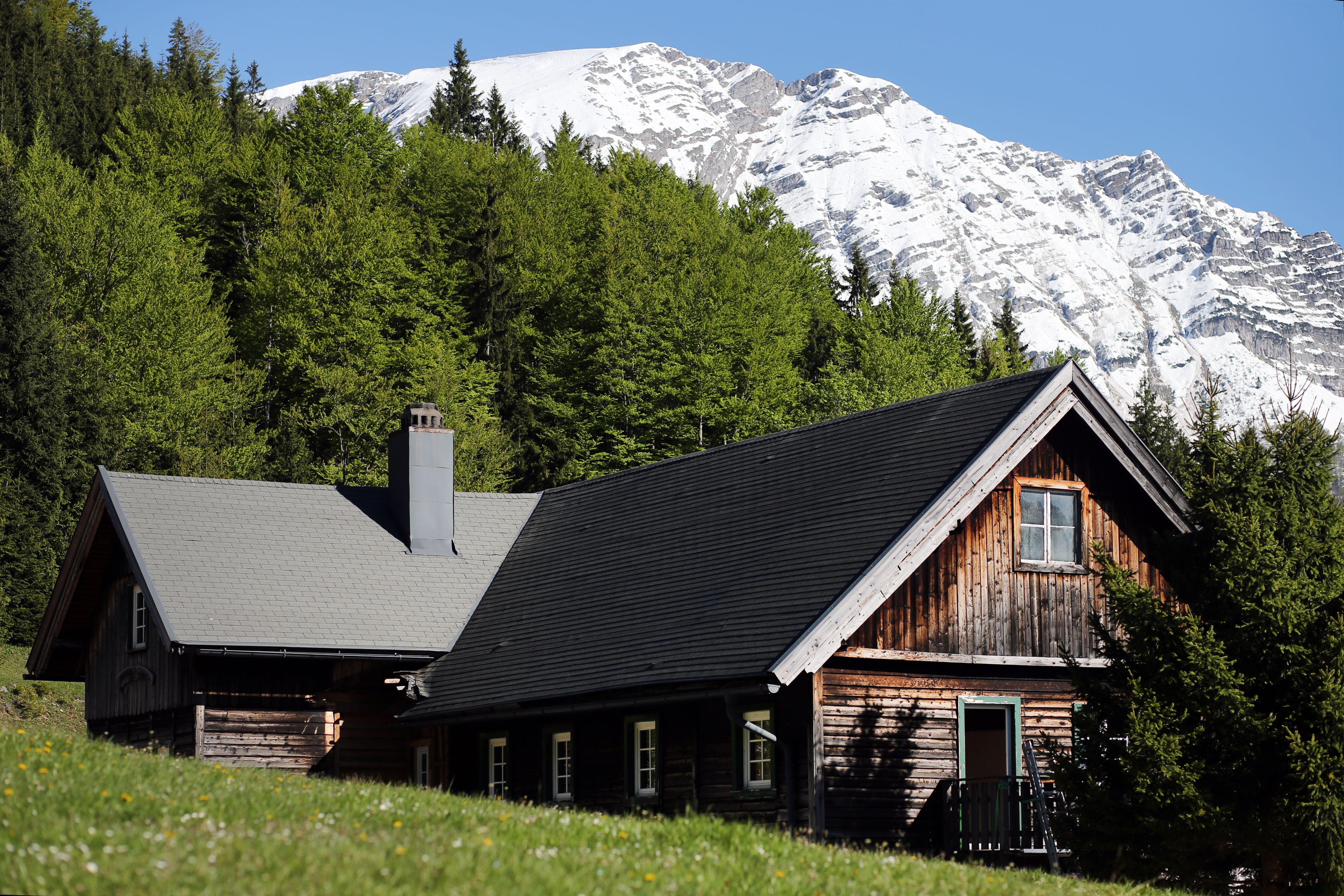 Wooden hut in front of a snow-covered mountain and green forest.