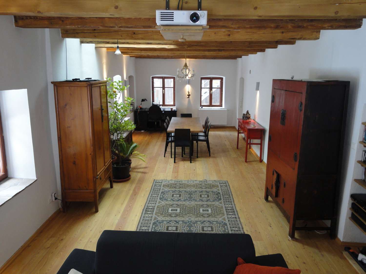 A stylishly furnished room with wooden floor, wooden beamed ceiling, antique furniture and a carpet.