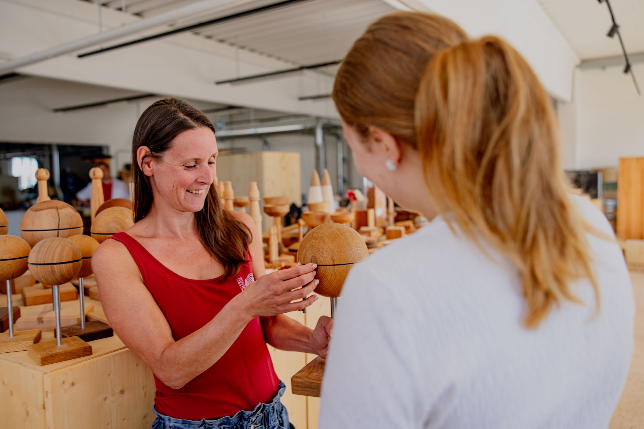 Two women look at a wooden object in a workshop.
