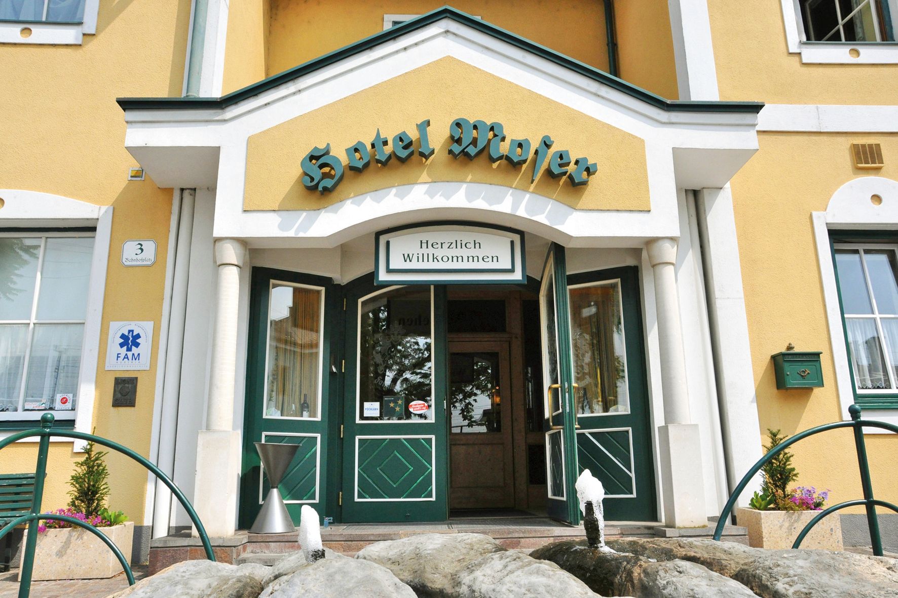 Entrance to Hotel Moser with yellow façade and green doors.