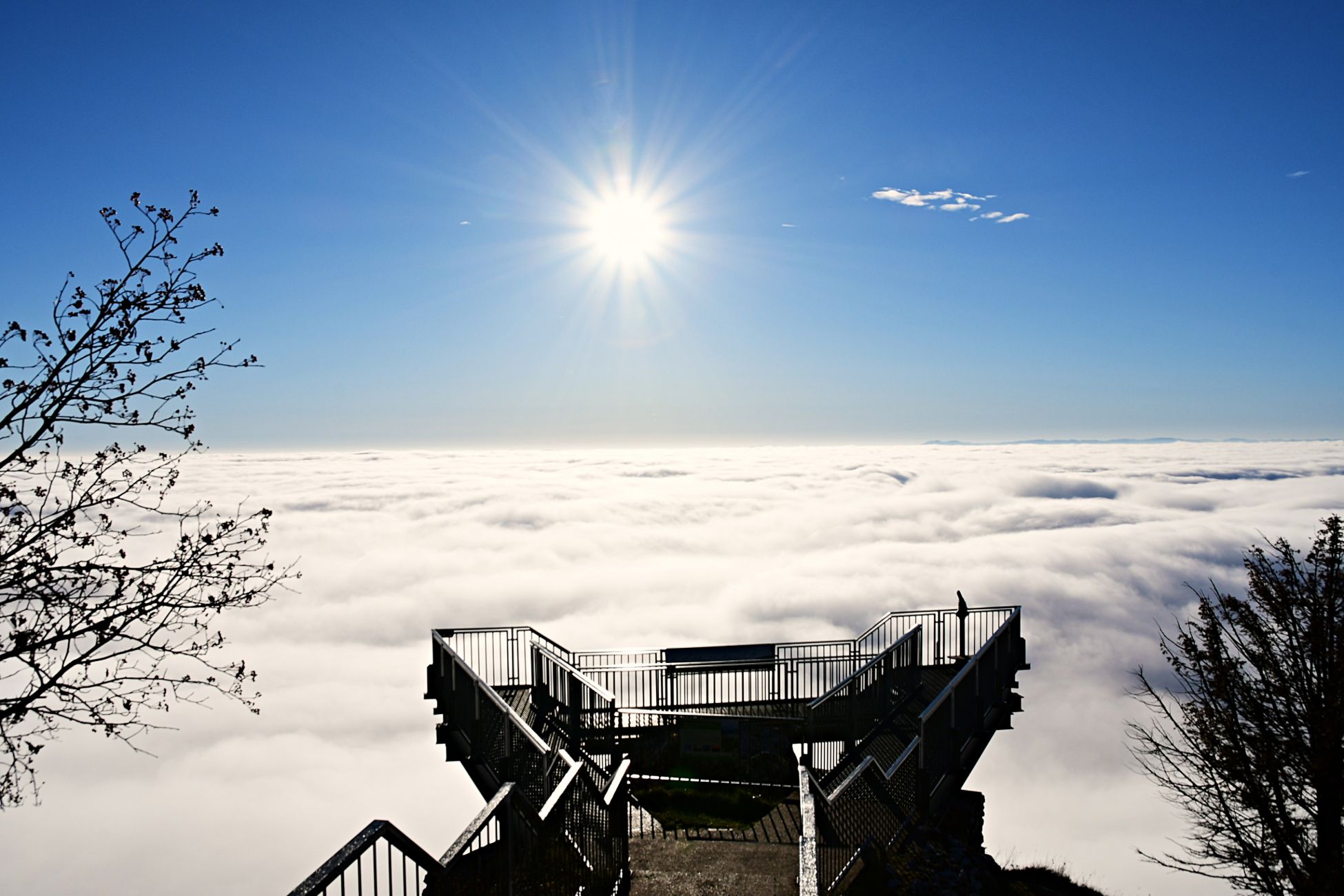 Viewing platform above a cloud cover with bright sun in the blue sky.