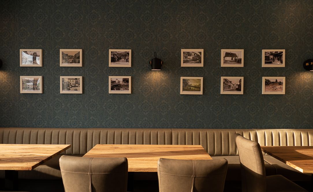 Interior view of a restaurant with upholstered benches and wooden tables, decorated with framed photos on the wall.