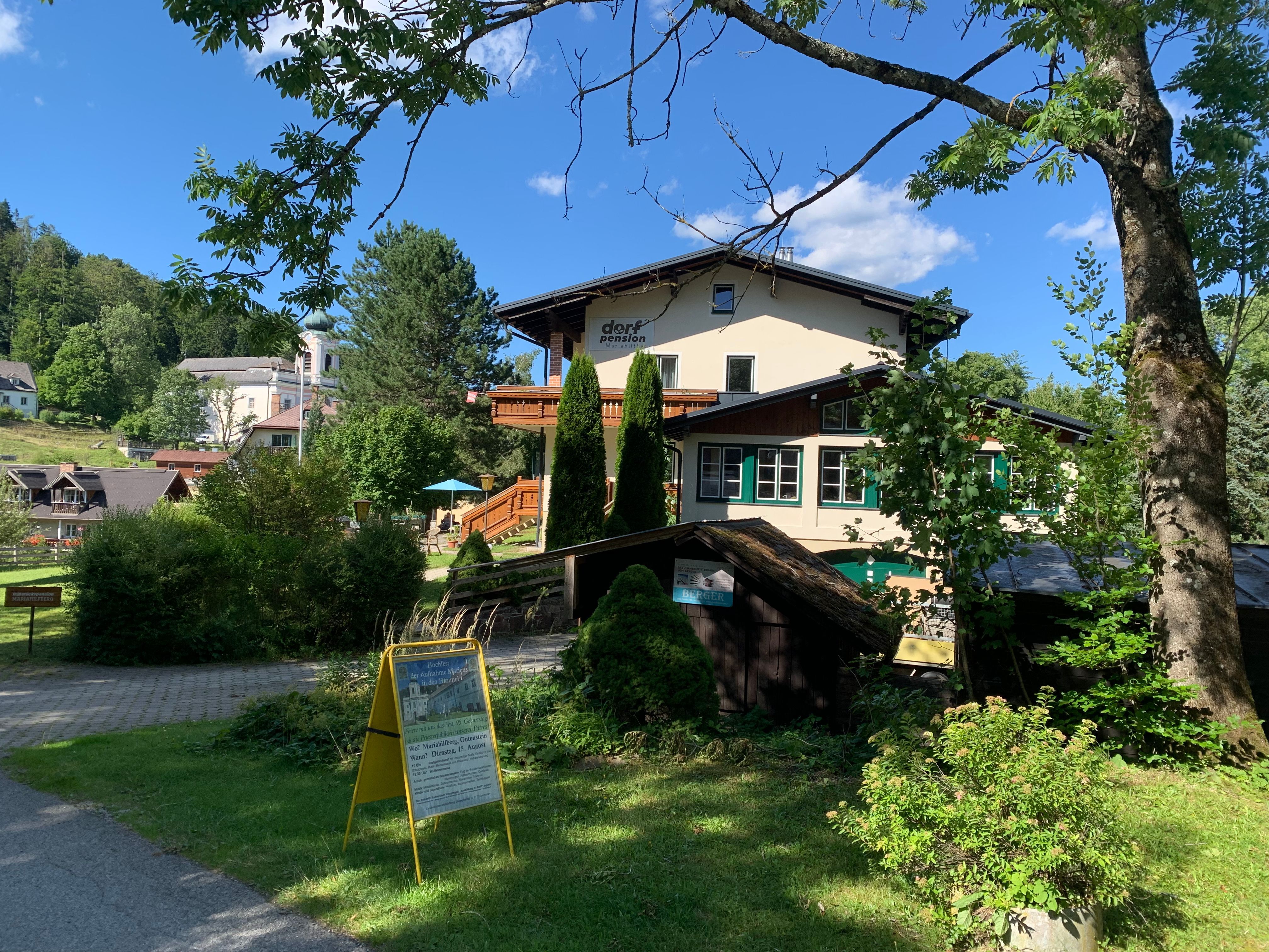A village guesthouse in a green, rural setting with trees and a blue sky.