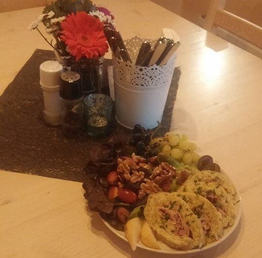 A plate of cold cuts, nuts, grapes and bread on a table with flowers and spices.