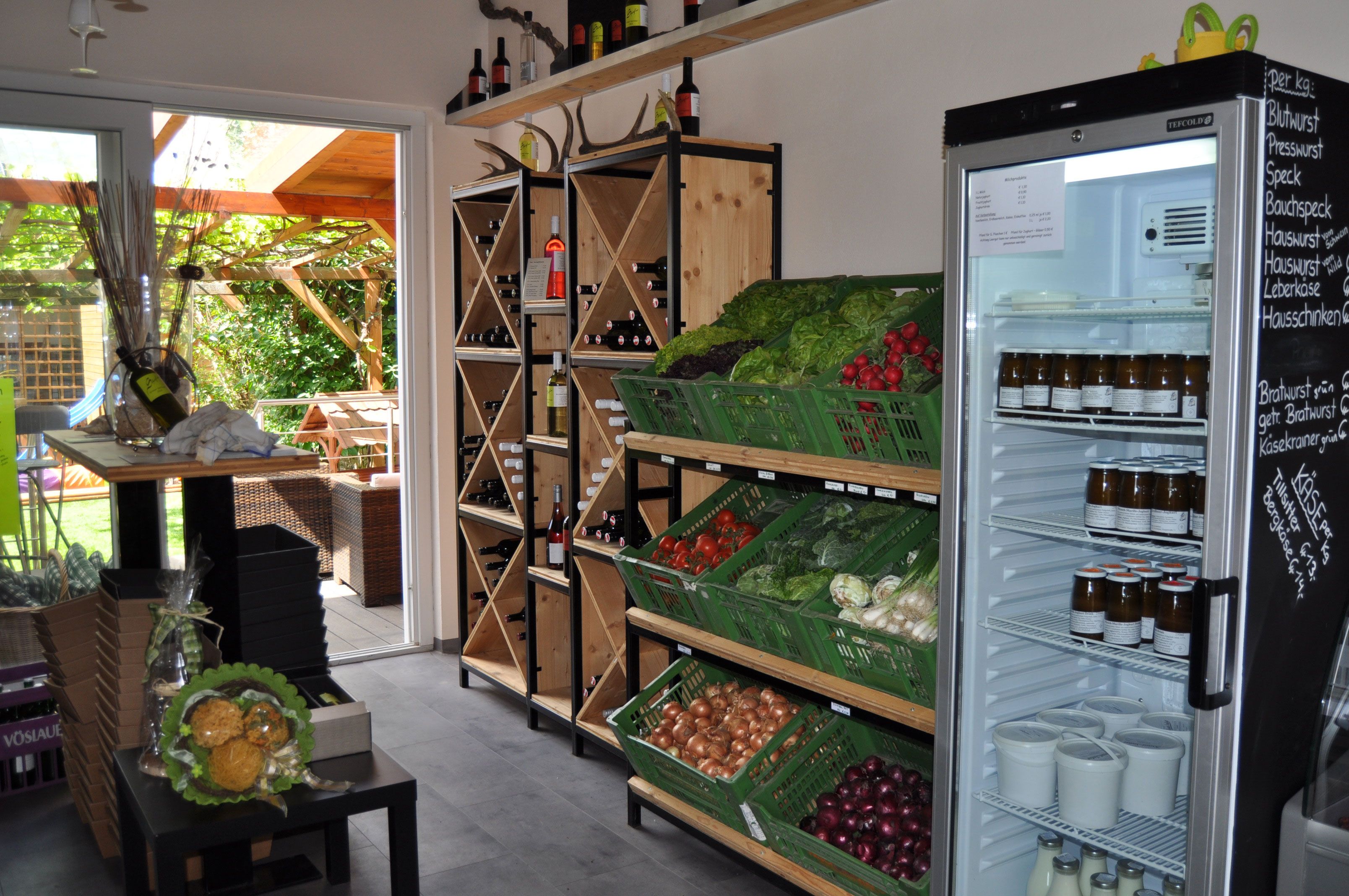 Interior view of a farm store with vegetables, wine shelves and refrigerator.