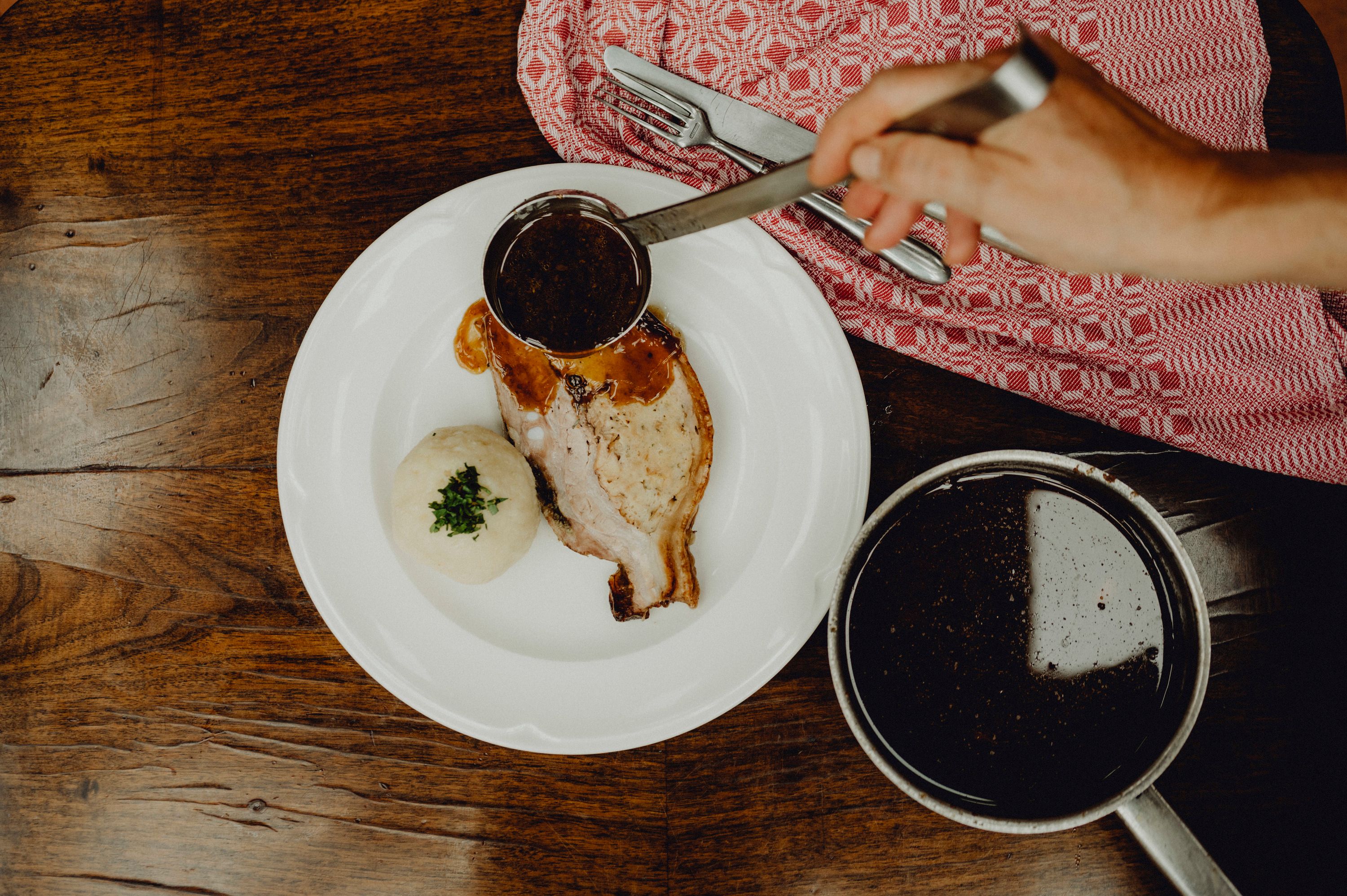 A plate of caraway roast and potato dumplings, covered in gravy, on a wooden table.