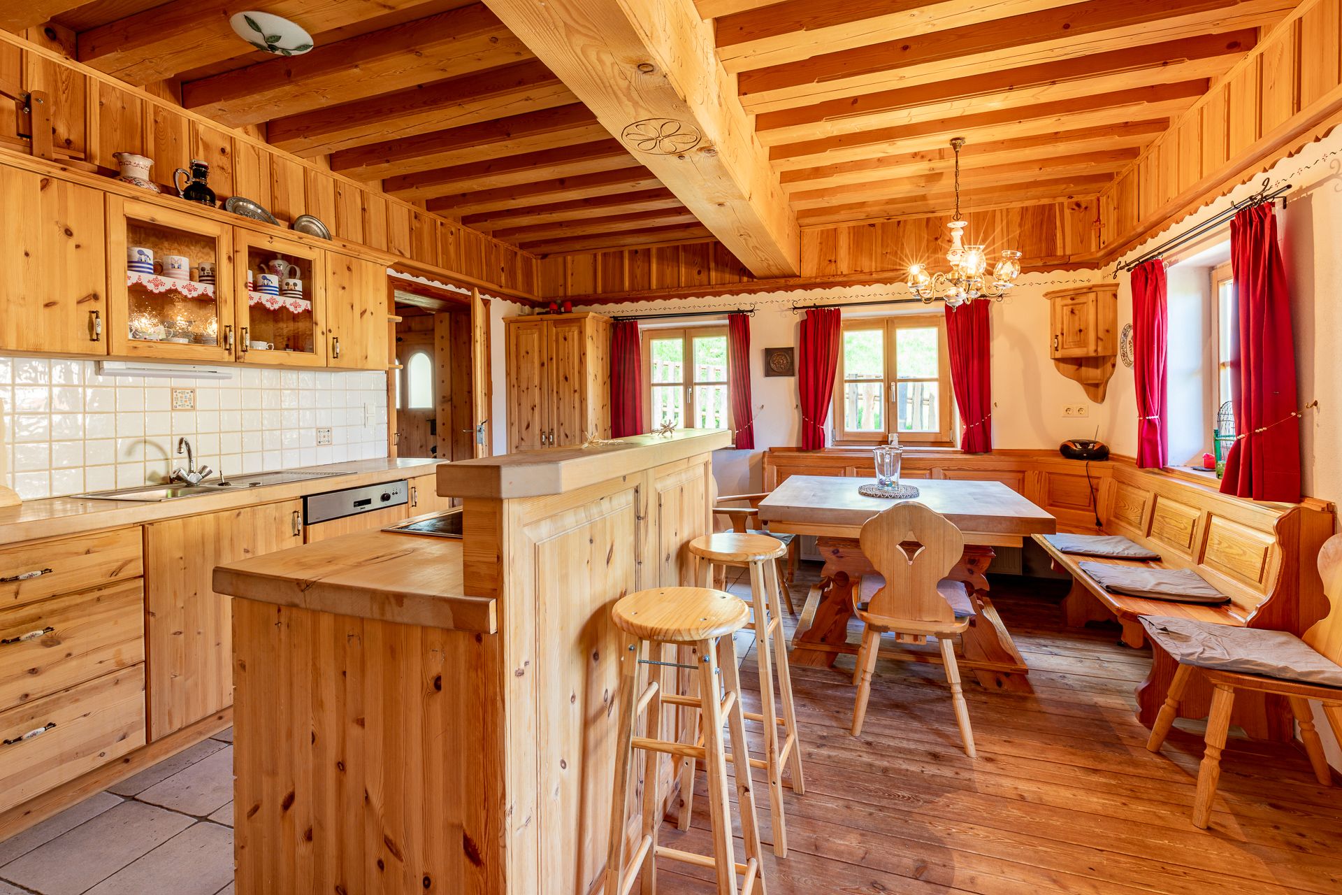 Traditional wooden kitchen with dining table, bench, chairs and red curtains.