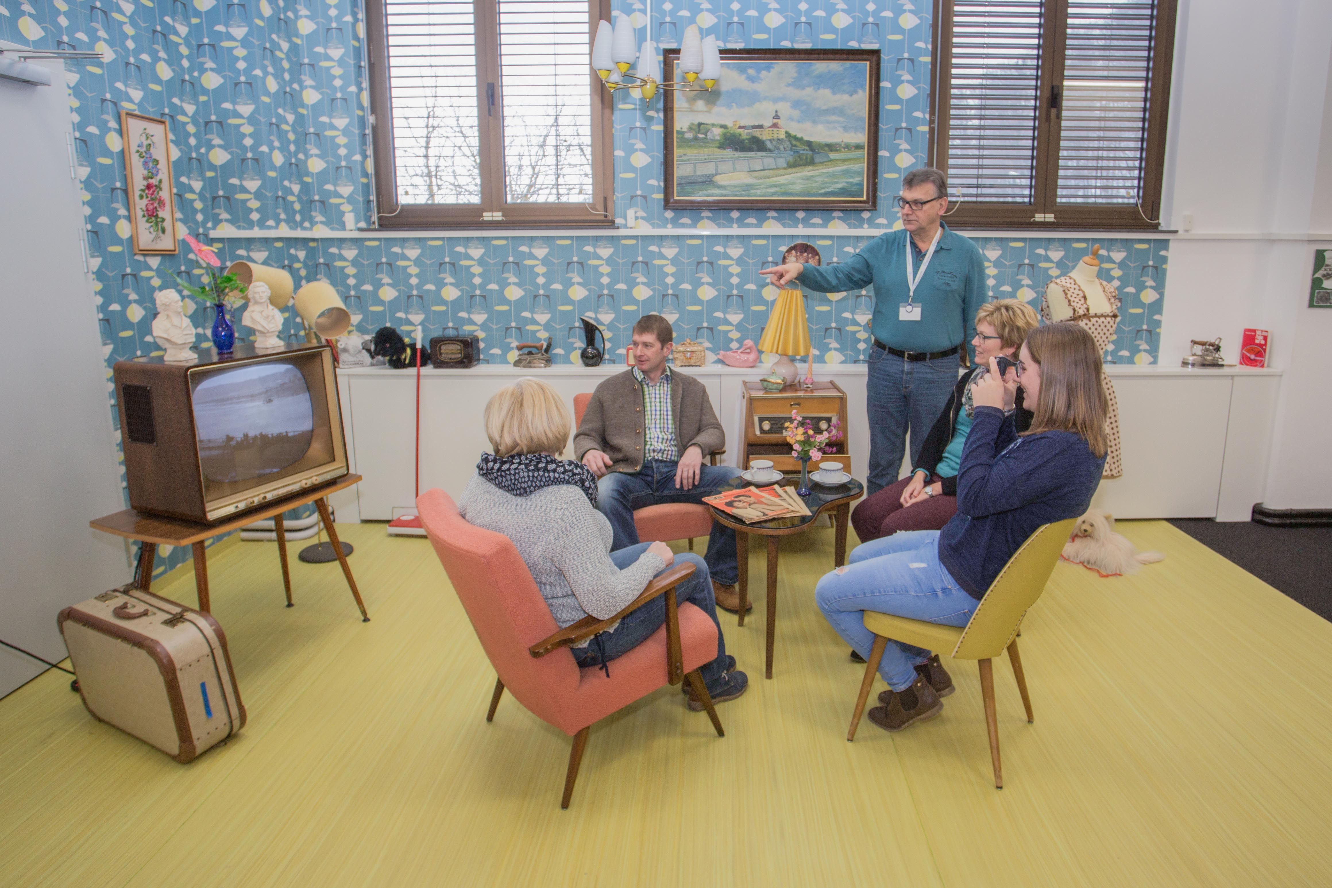 Group of people in a 60's style living room with retro furniture and decoration.
