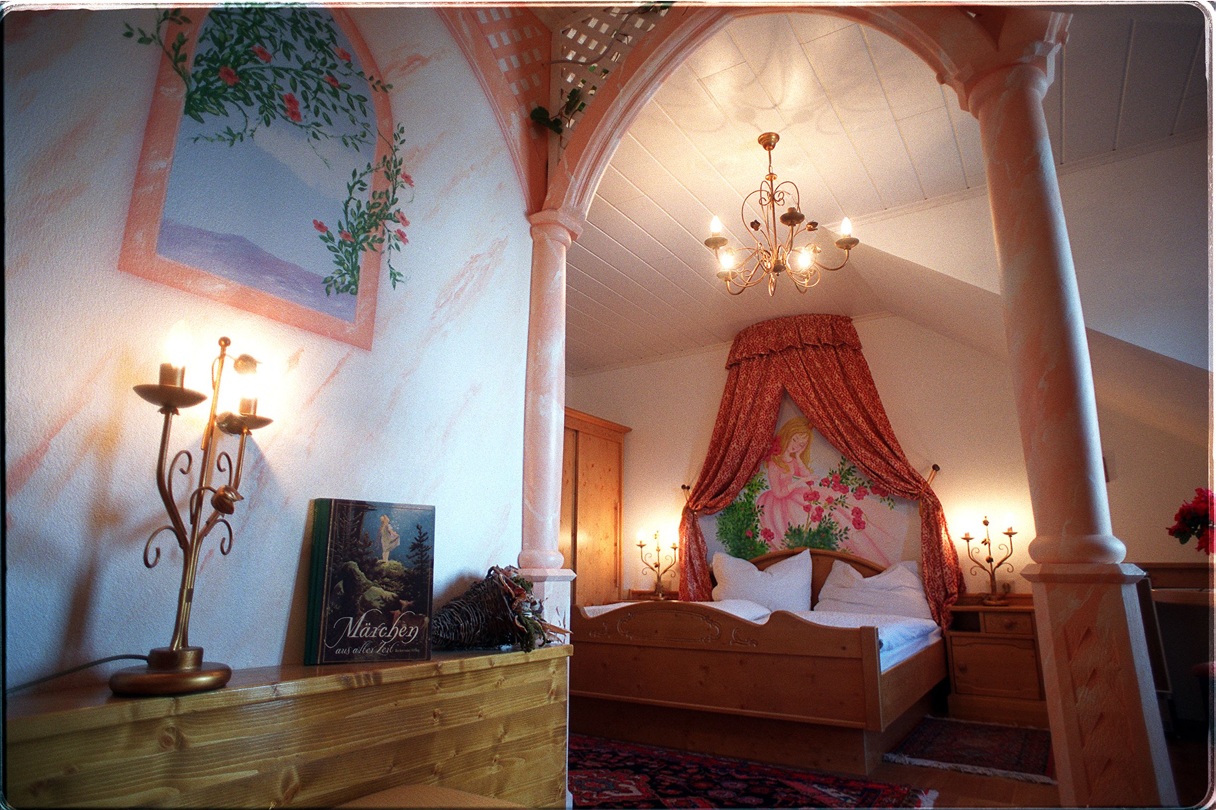 A romantically decorated bedroom with a canopy, candlesticks and a fairytale book on a shelf.
