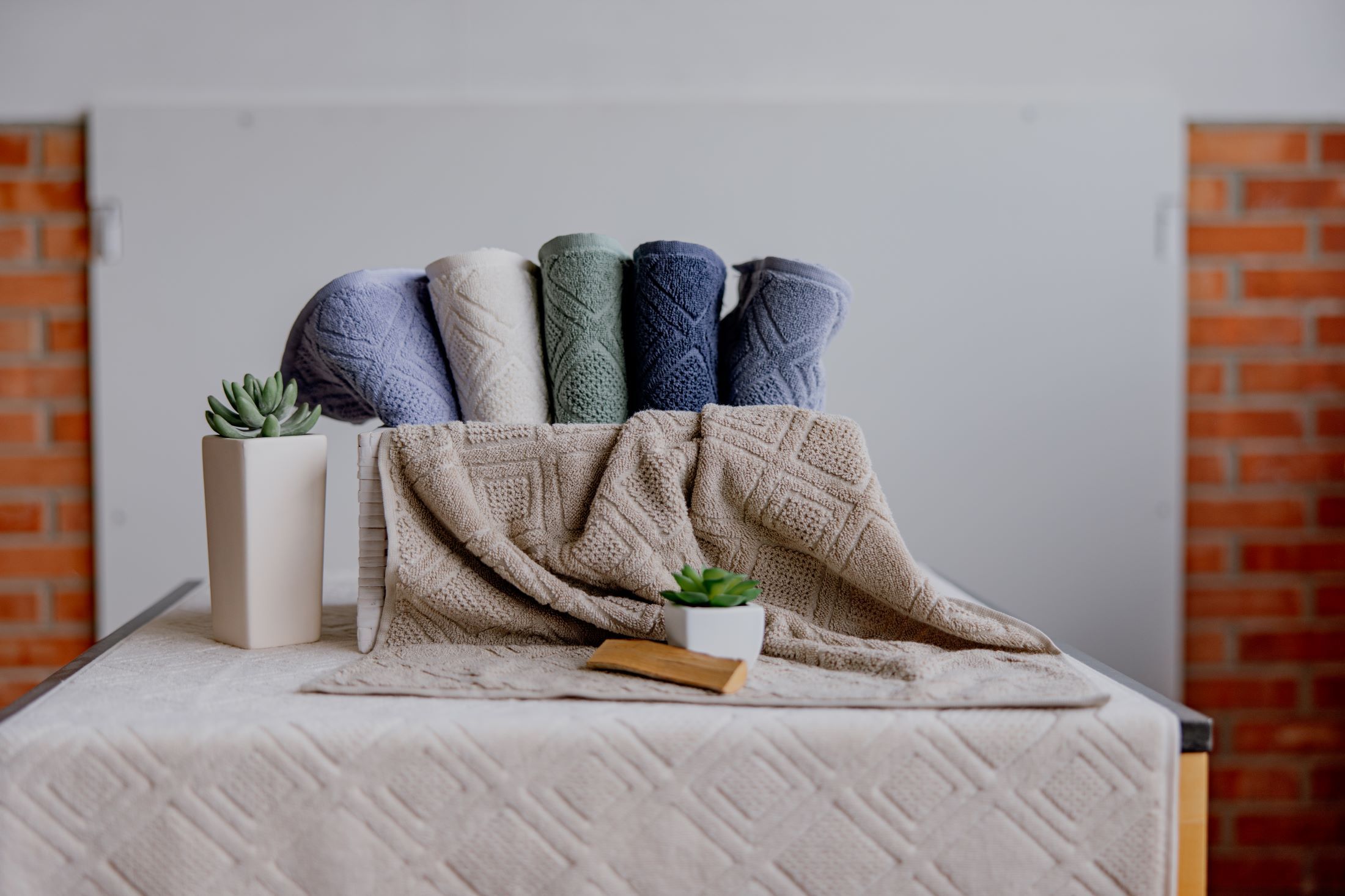 Colored towels and plants on a table in front of a brick wall.