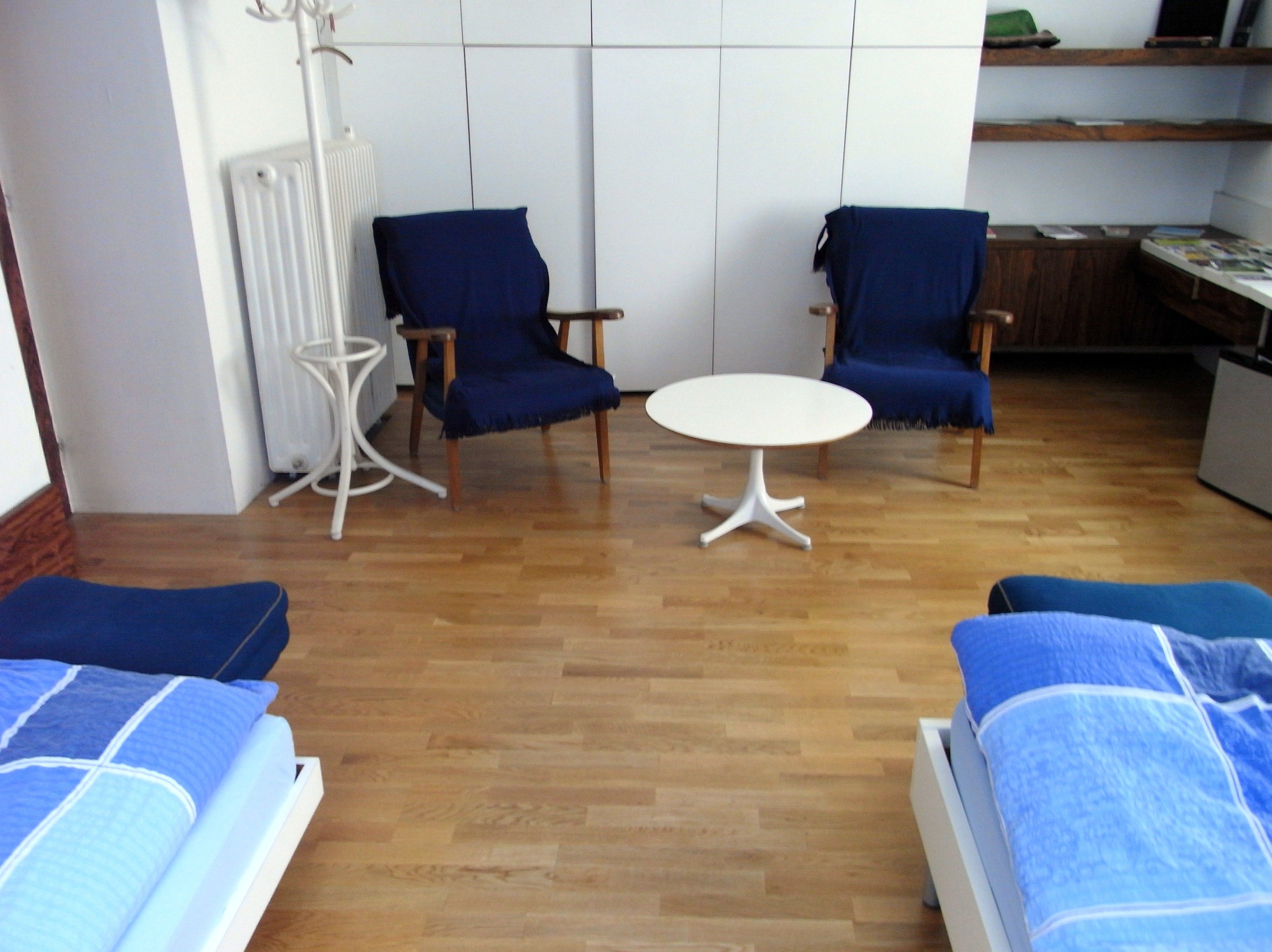 A room with two blue armchairs, a white round table and two beds with blue bed linen on a wooden floor.